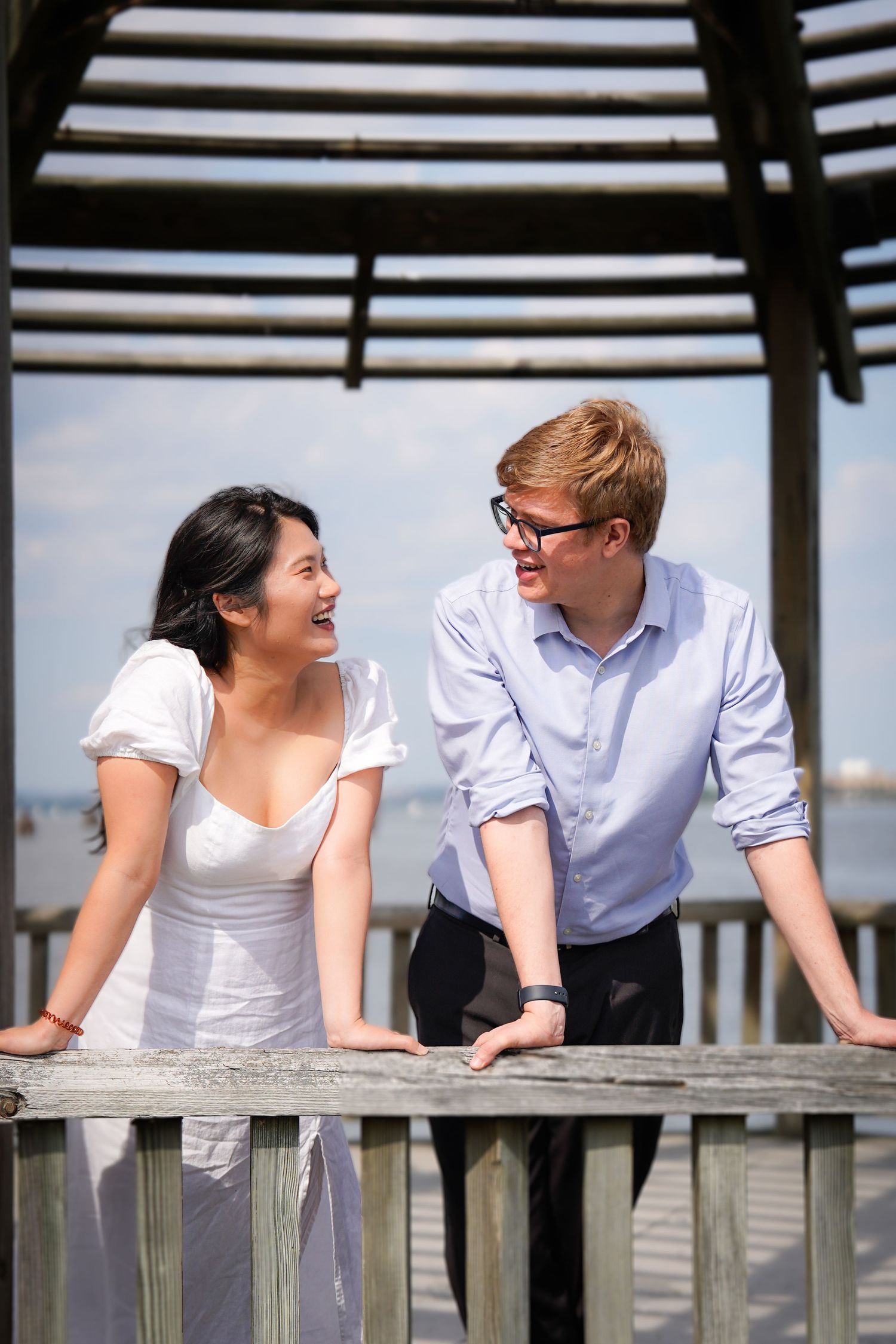 A couple leans on a wooden railing while sharing joyful moments together.