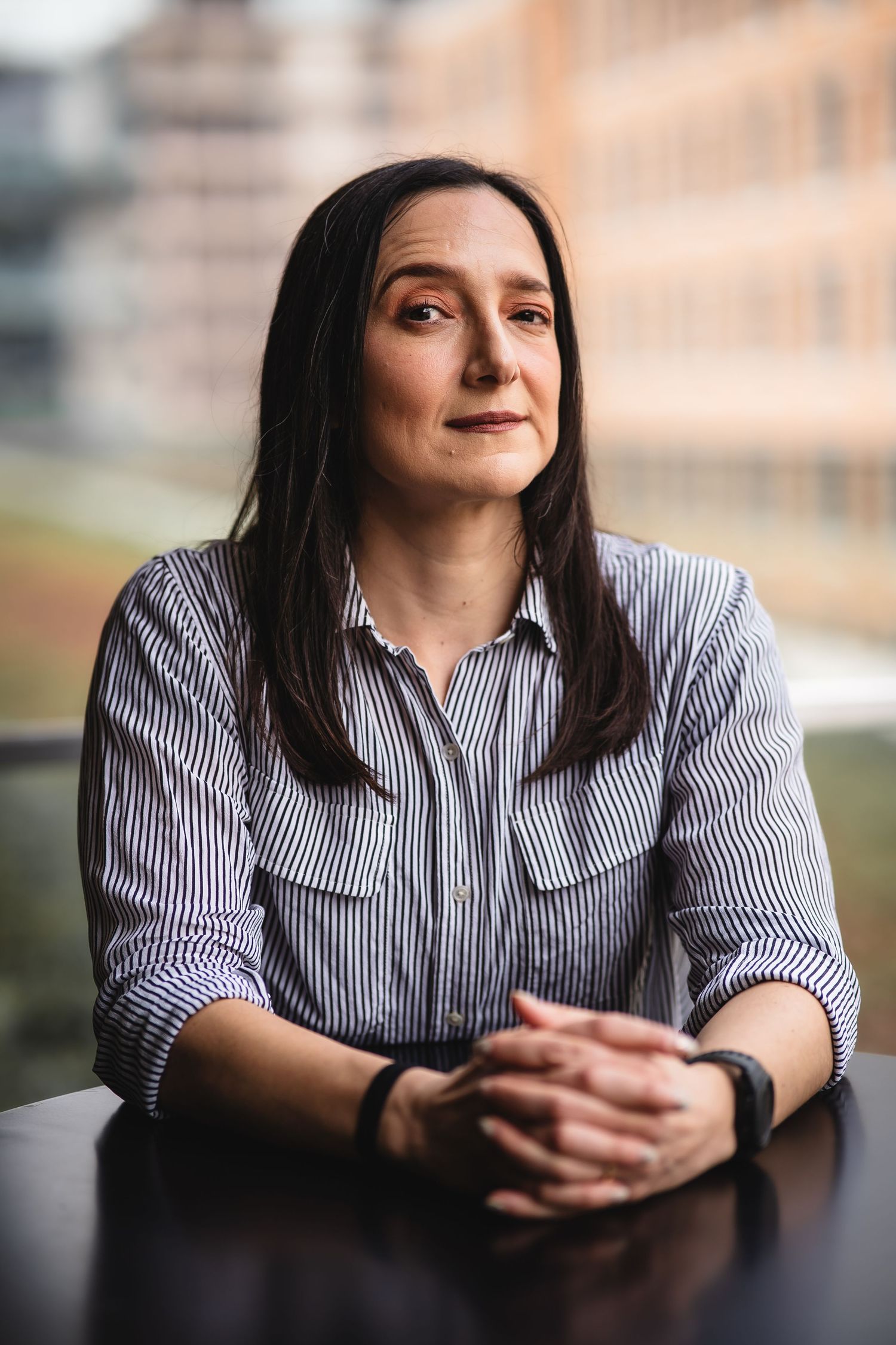 Professional portrait of person in striped button-down shirt leaning on dark surface.