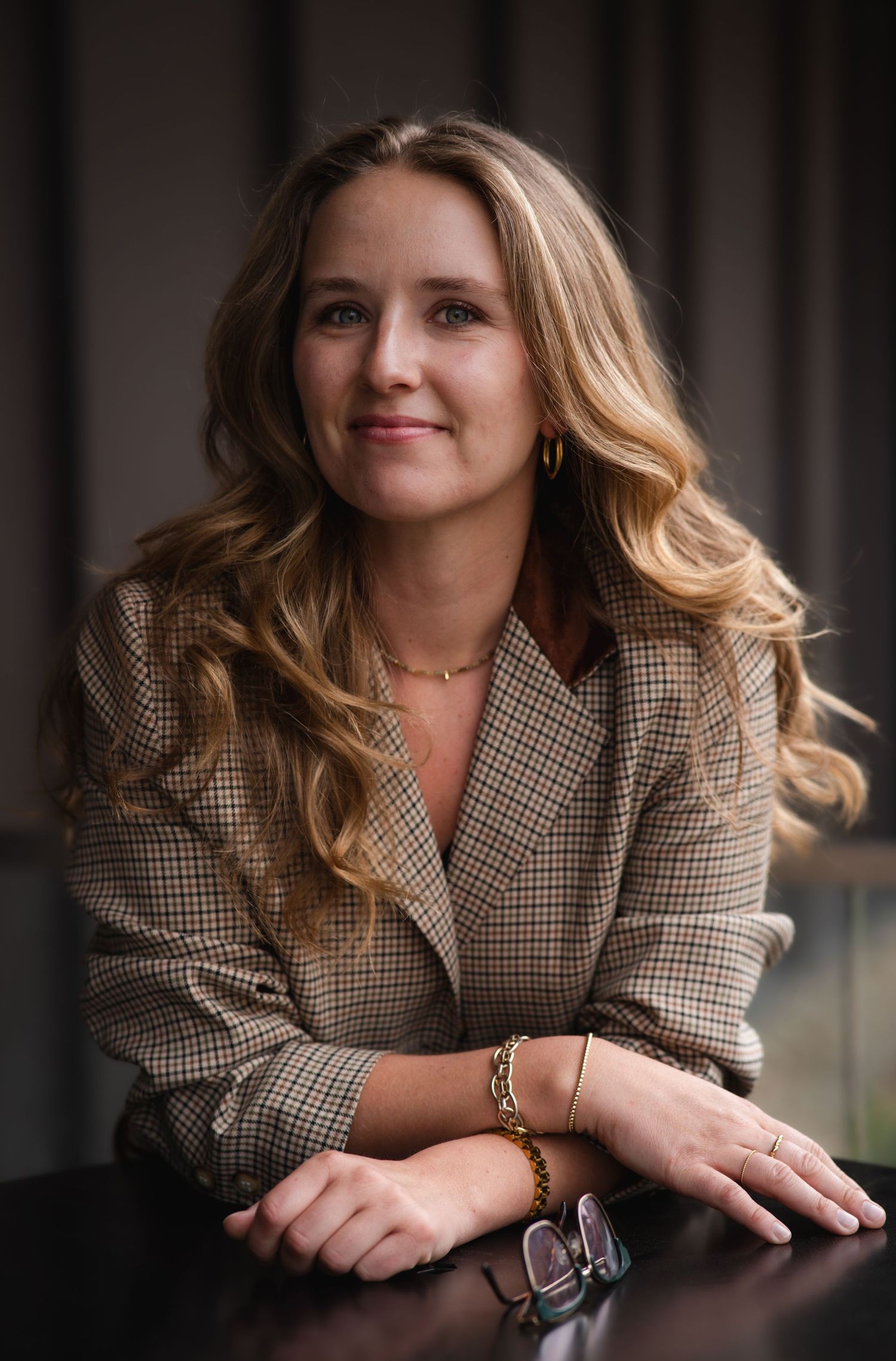 Professional headshot of someone in a plaid blazer leaning forward with a warm expression.