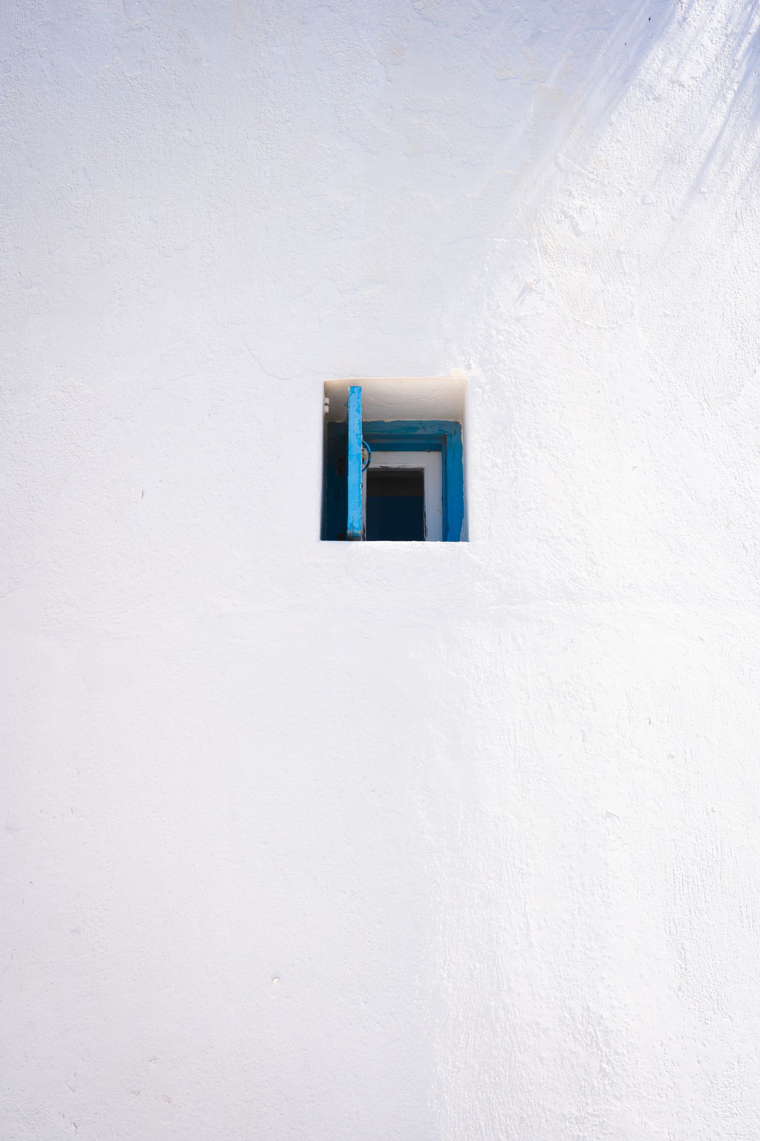 Minimalist architectural detail showing a small blue window frame against a stark white wall in a geometric composition.