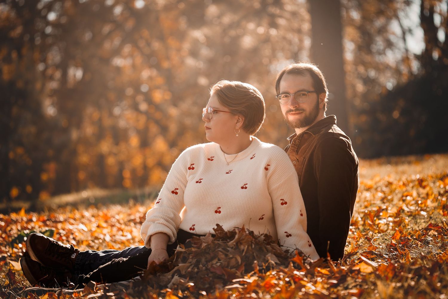 A couple lying together on autumn leaves during a golden sunset photoshoot.