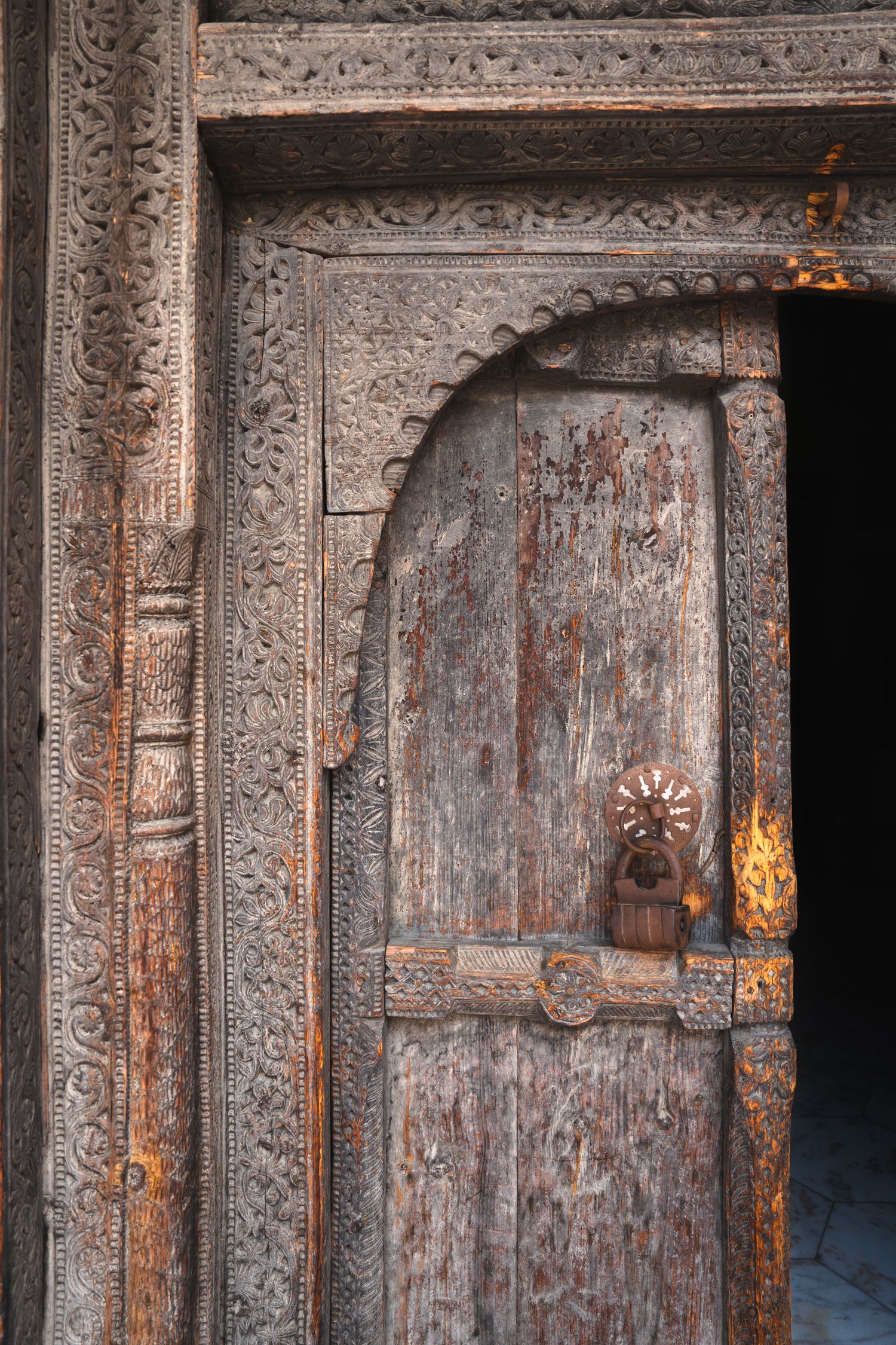 Ancient wooden door with intricate stone carvings and ornate metal details in a traditional architectural doorway.