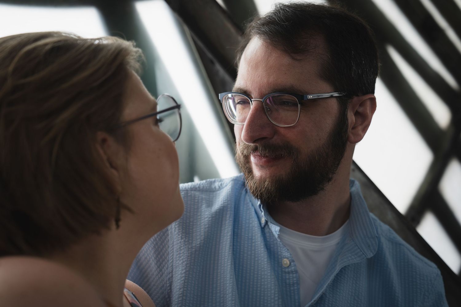 A couple wearing glasses share a tender moment in front of a clock background.