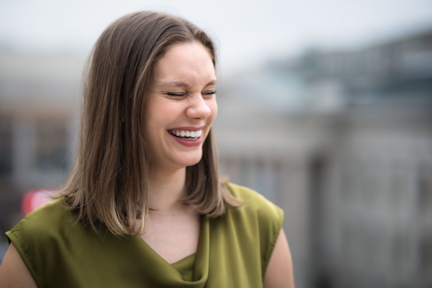 Person in olive green top smiles brightly during outdoor photoshoot.
