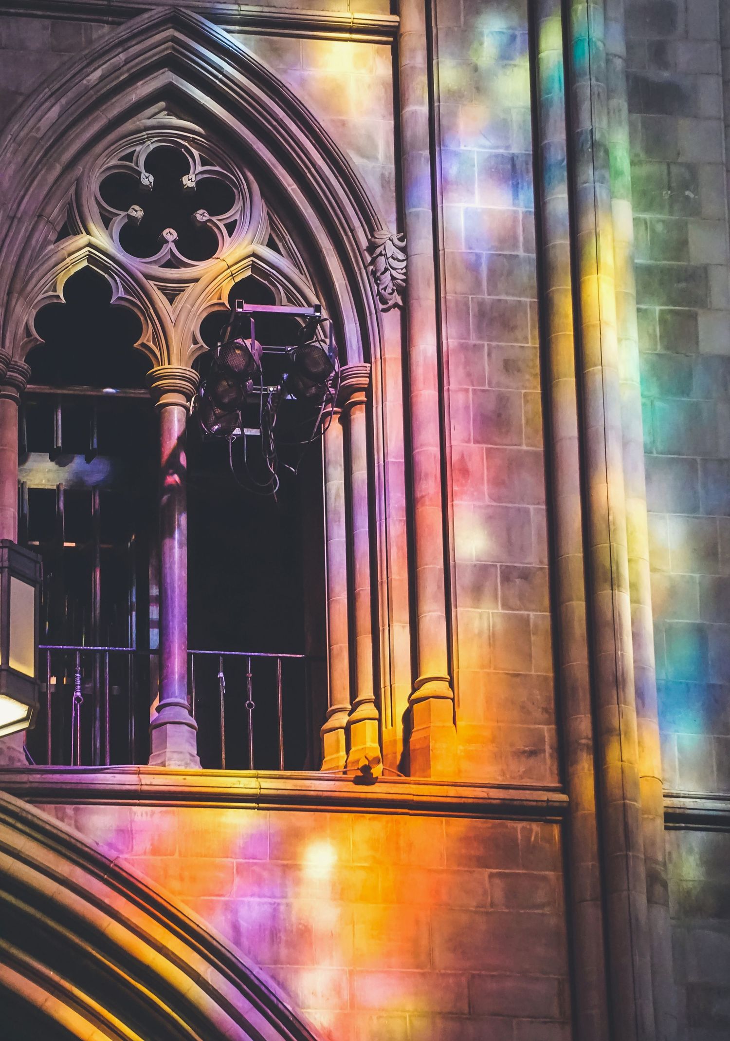 Gothic church interior with colorful stained glass light reflections on stone archways.