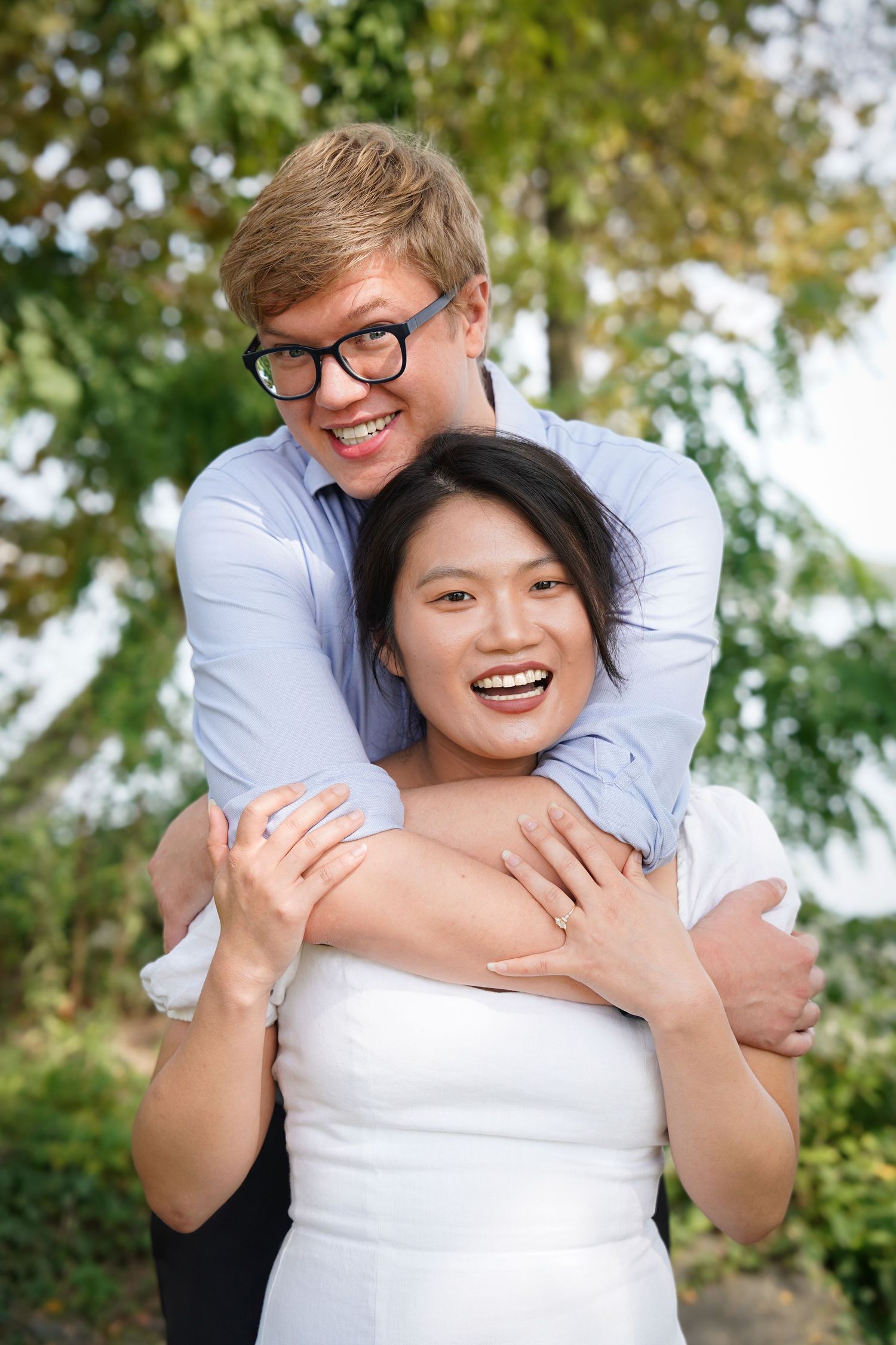 A playful embrace captured in a sunny outdoor setting with trees in the background.