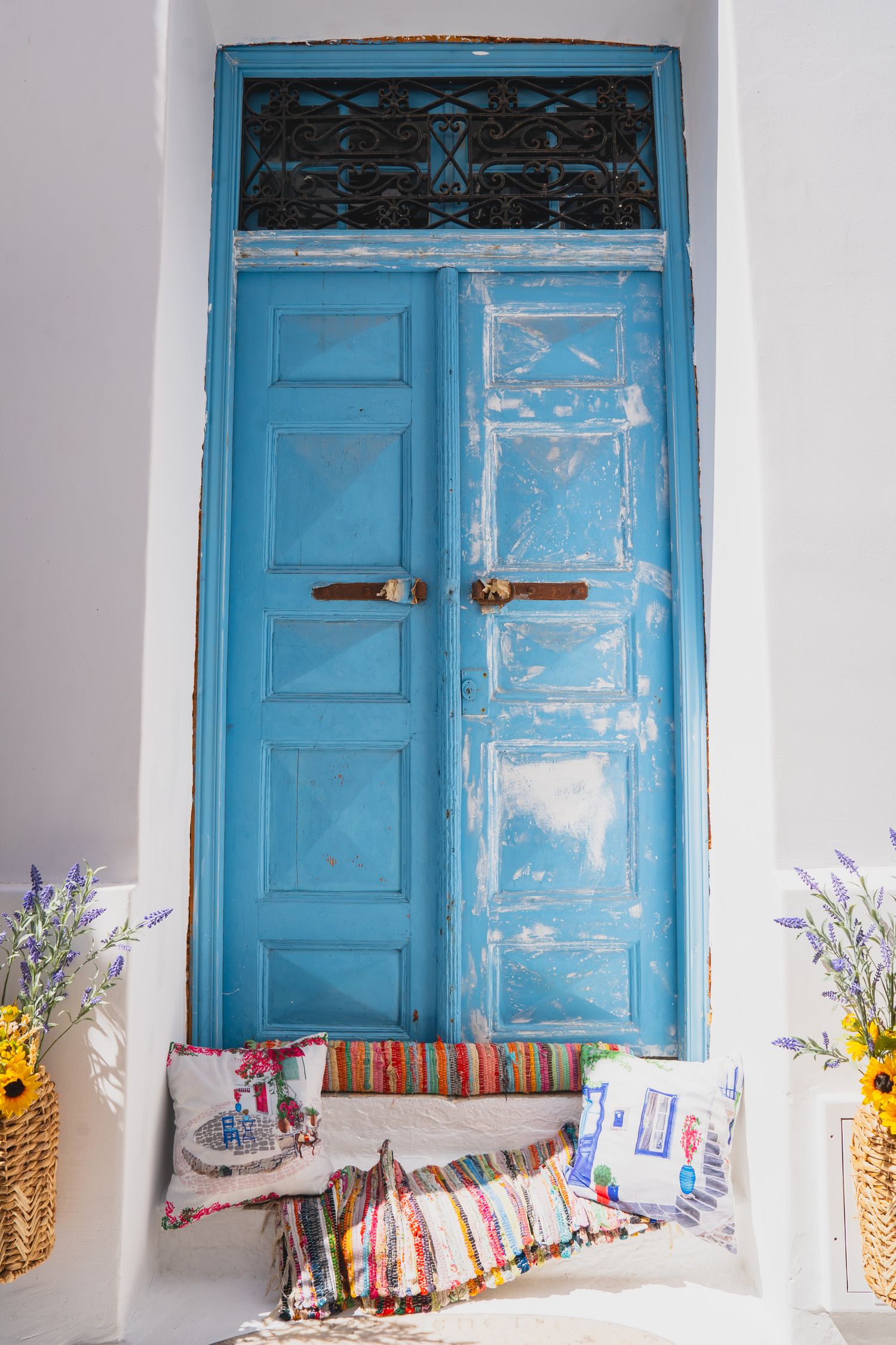 Blue traditional doors with decorative cushions and floral arrangements in Mediterranean style.