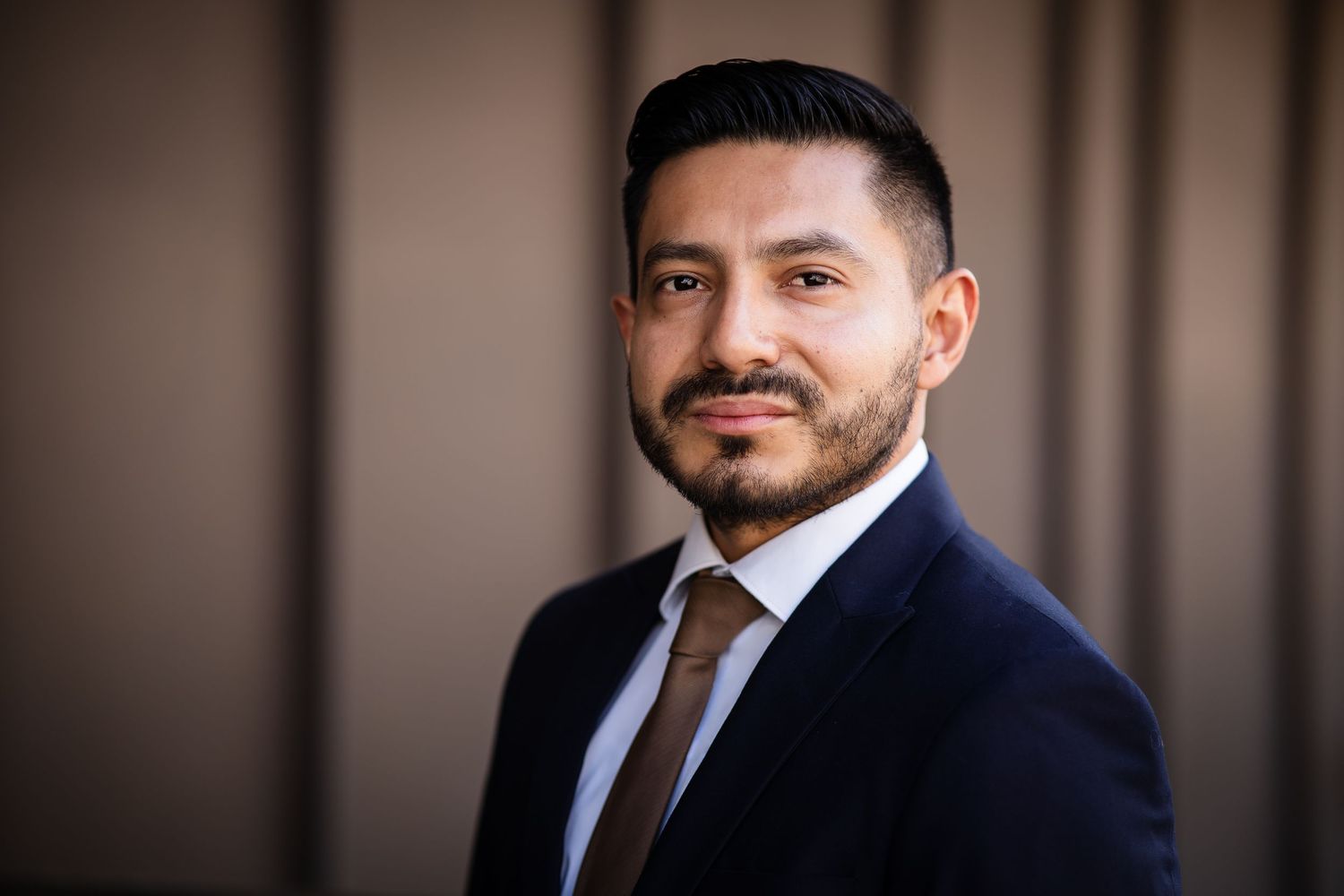 Professional in navy suit and brown tie poses for corporate headshot.