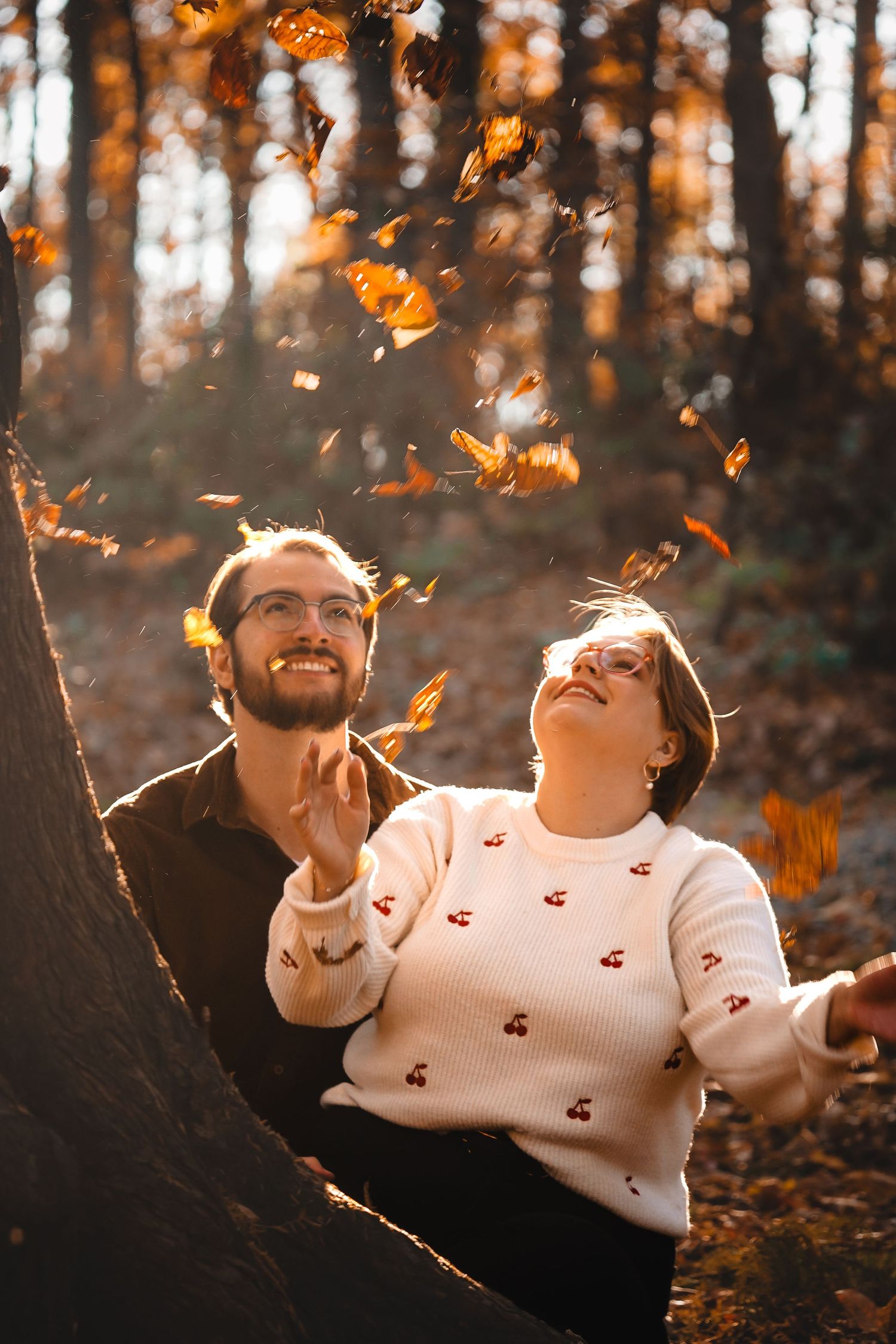 A couple throws autumn leaves in the air during a sunset photoshoot.