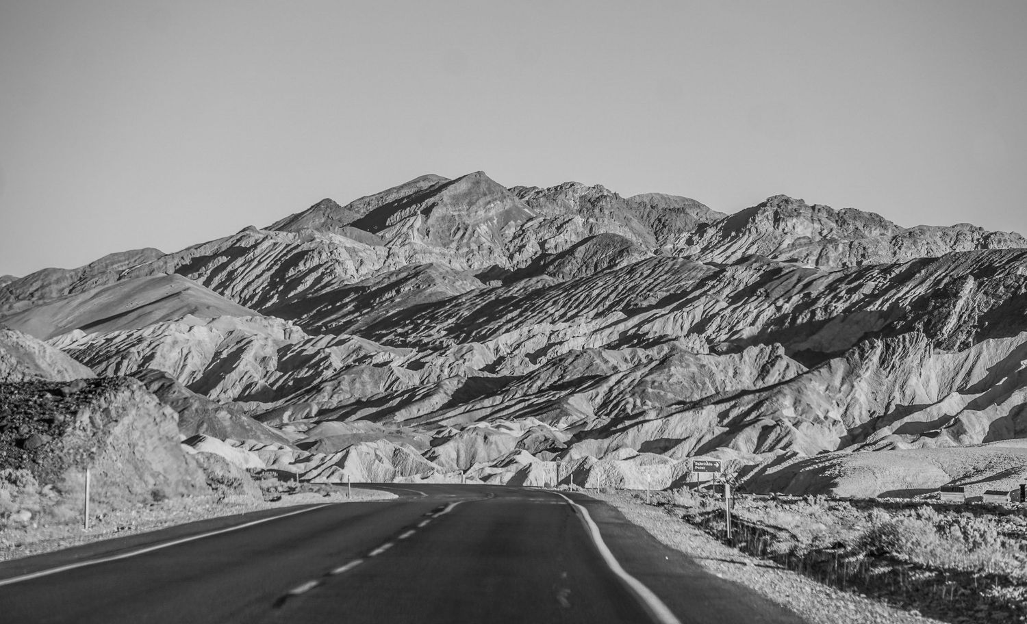 Winding desert road through rugged mountain terrain in black and white landscape photography.