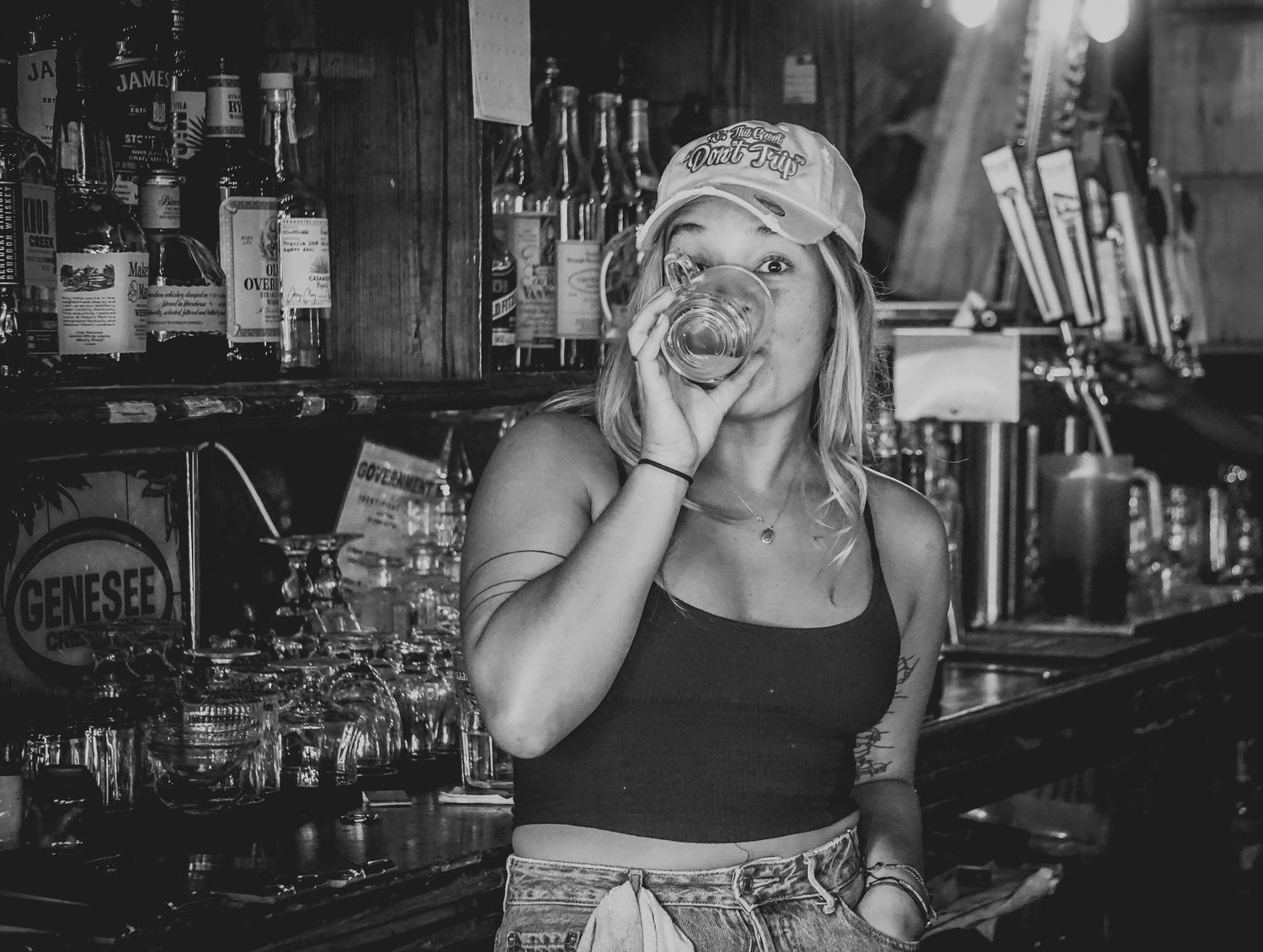 Bartender in baseball cap making expressive face behind bar counter.