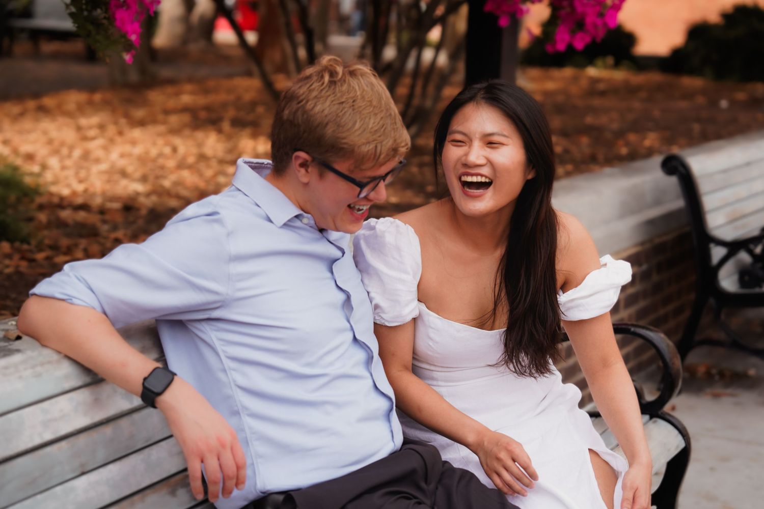 Playful couple laughing and embracing on wooden benches during sunset.