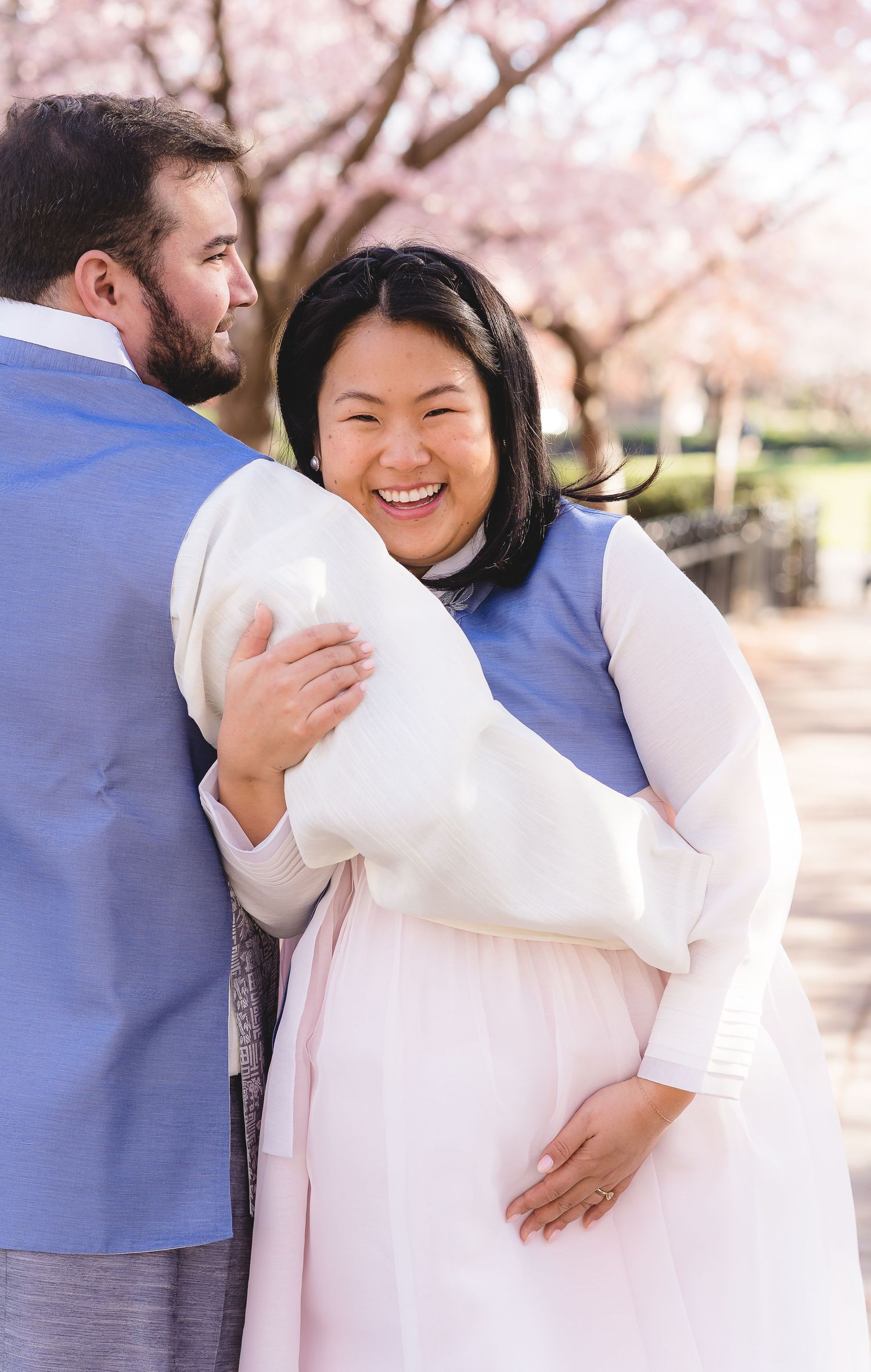 A couple embraces under delicate pink cherry blossoms on a bright spring day.