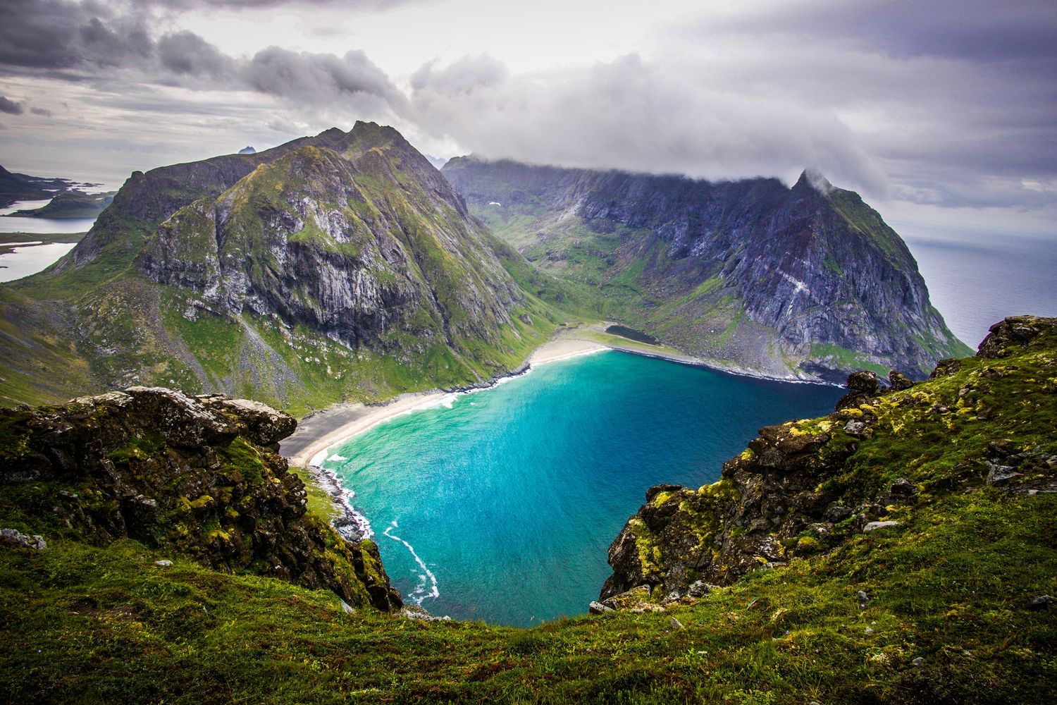 Dramatic aerial view of a turquoise bay surrounded by steep mountain cliffs in the Lofoten Islands.