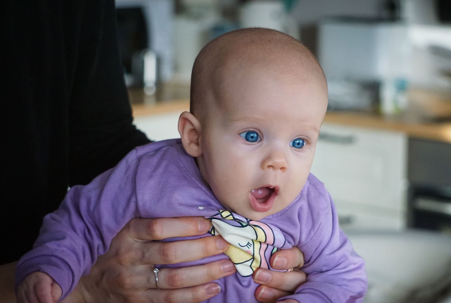 Baby in purple outfit making expressive faces during mealtime.