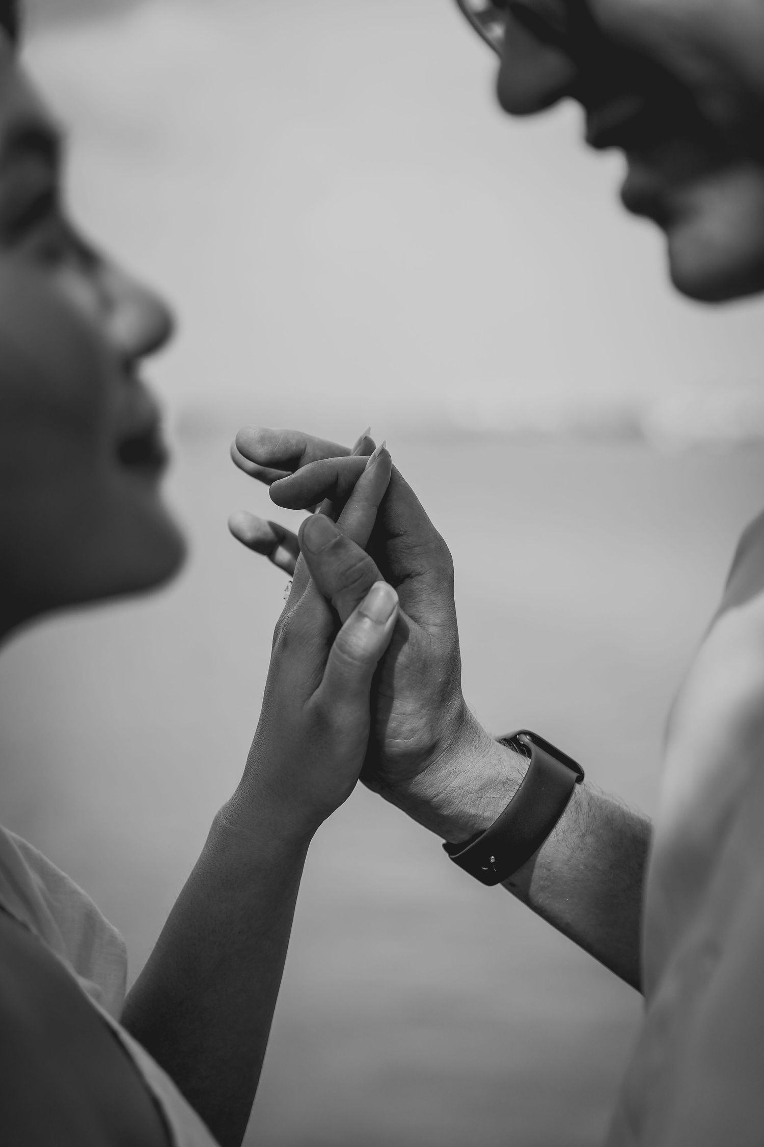 Black and white close-up of hands intertwined in an intimate gesture.
