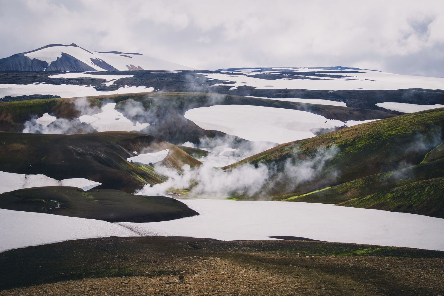 Snow-covered volcanic landscape with steam rising from geothermal vents in Iceland.