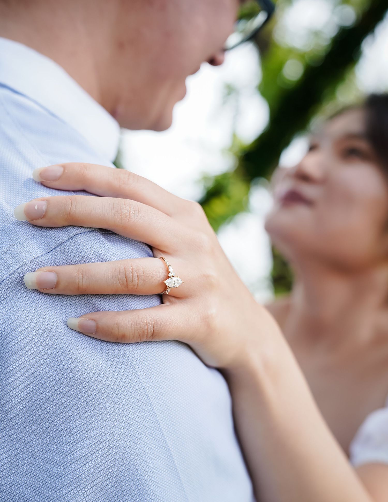 Close-up of hand with engagement ring resting gently on a light blue shirt.