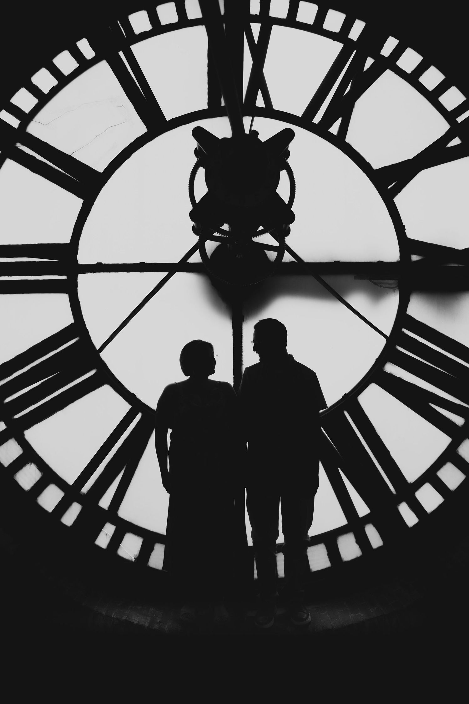 Silhouetted figures against a large clock face in dramatic black and white.