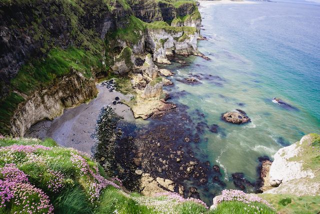 Dramatic coastal cliffs with turquoise water coves and rocky outcrops along a scenic shoreline.
