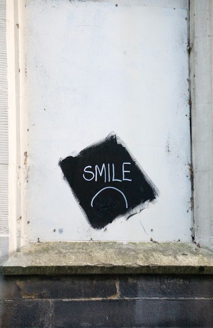 Minimalist graffiti on white wall spelling out 'SMILE' in simple black text.