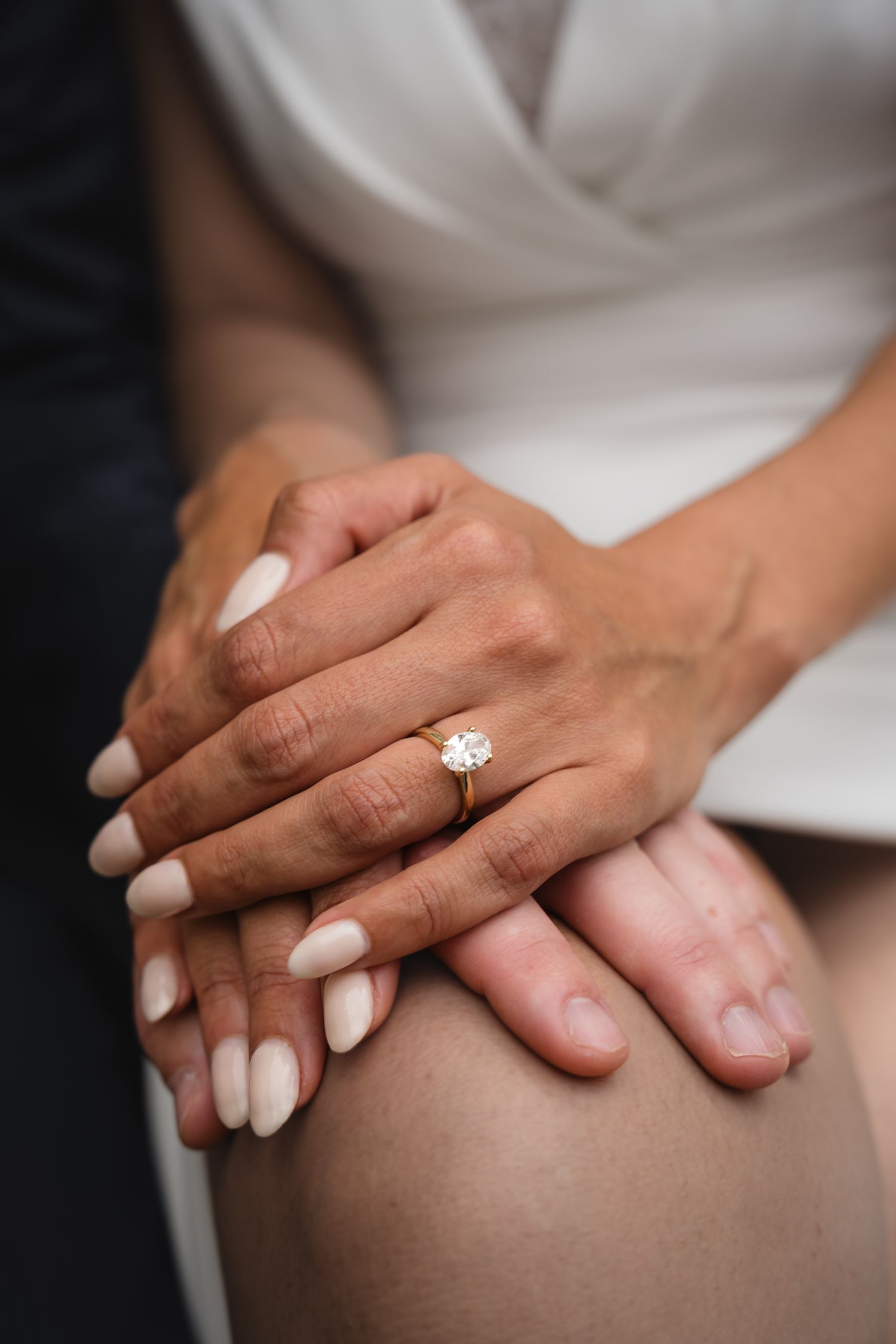 Close-up of a woman's hand wearing a gold diamond engagement ring, held tenderly by her partner's hand.