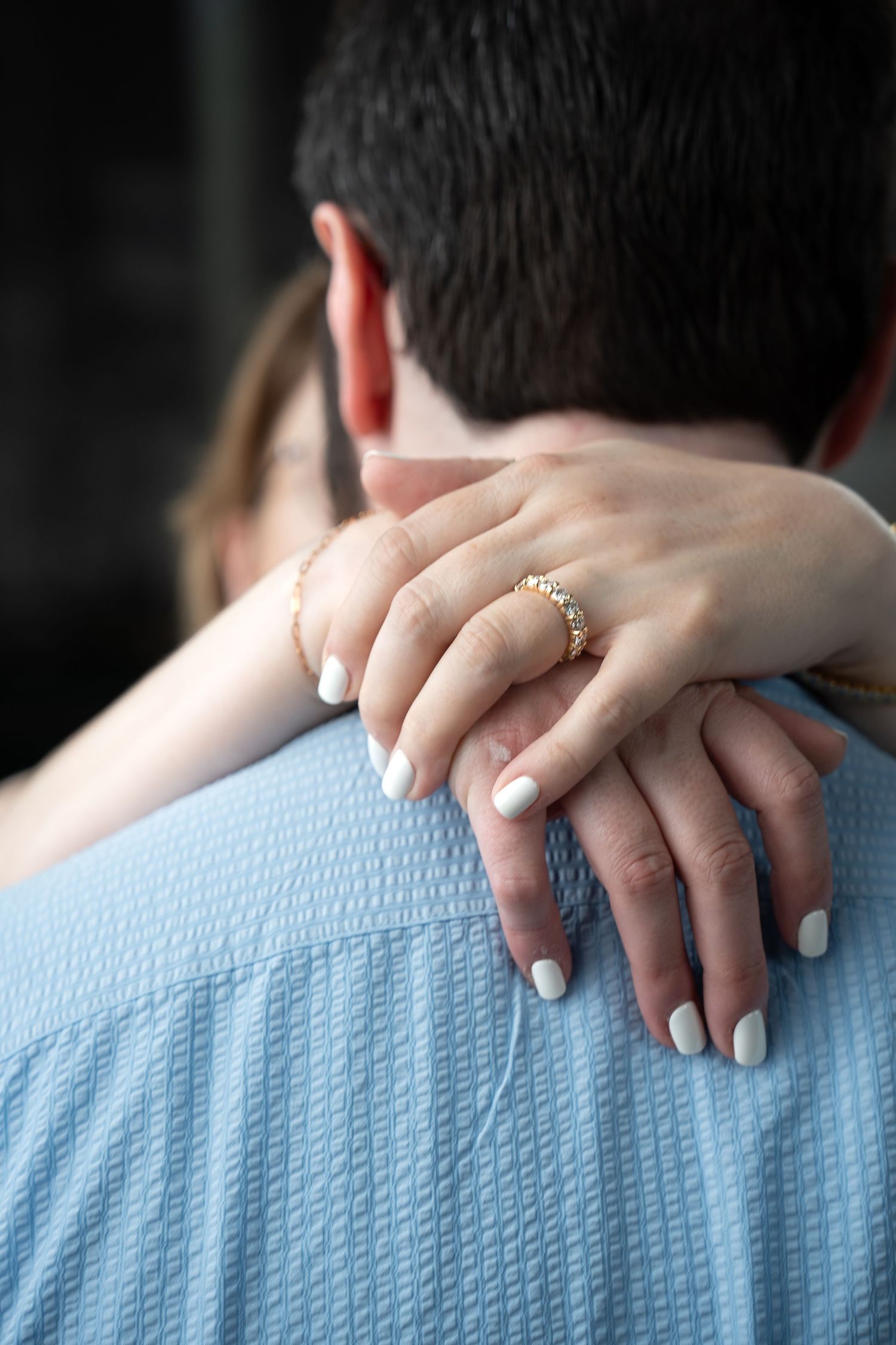 Close-up of hands with an engagement ring resting on a light blue shirt.