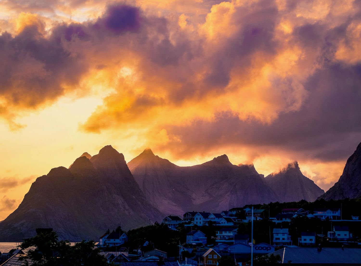 Mountain range silhouetted against dramatic orange and purple sunset sky with clouds.