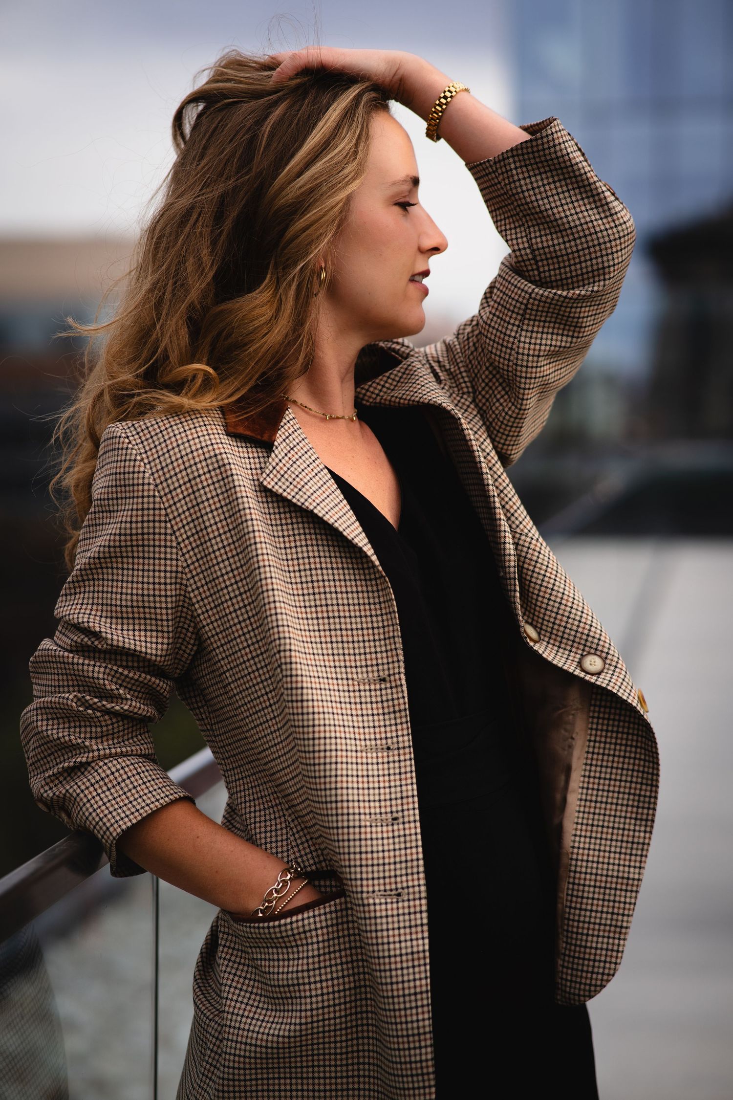 Fashion model wearing a brown plaid blazer poses against an urban backdrop.