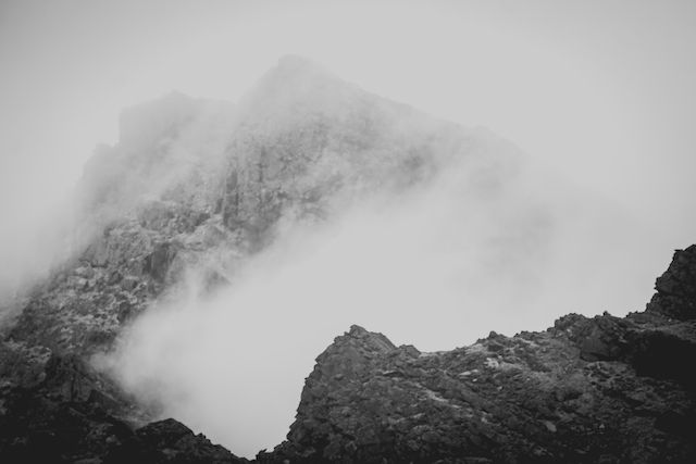 Misty mountain peaks shrouded in gray clouds creating a moody monochrome landscape.