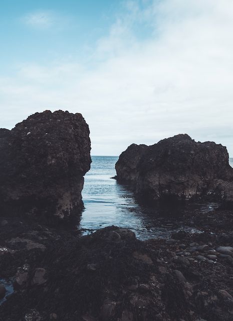 Rocky coastal landscape with dark volcanic formations against ocean and sky.