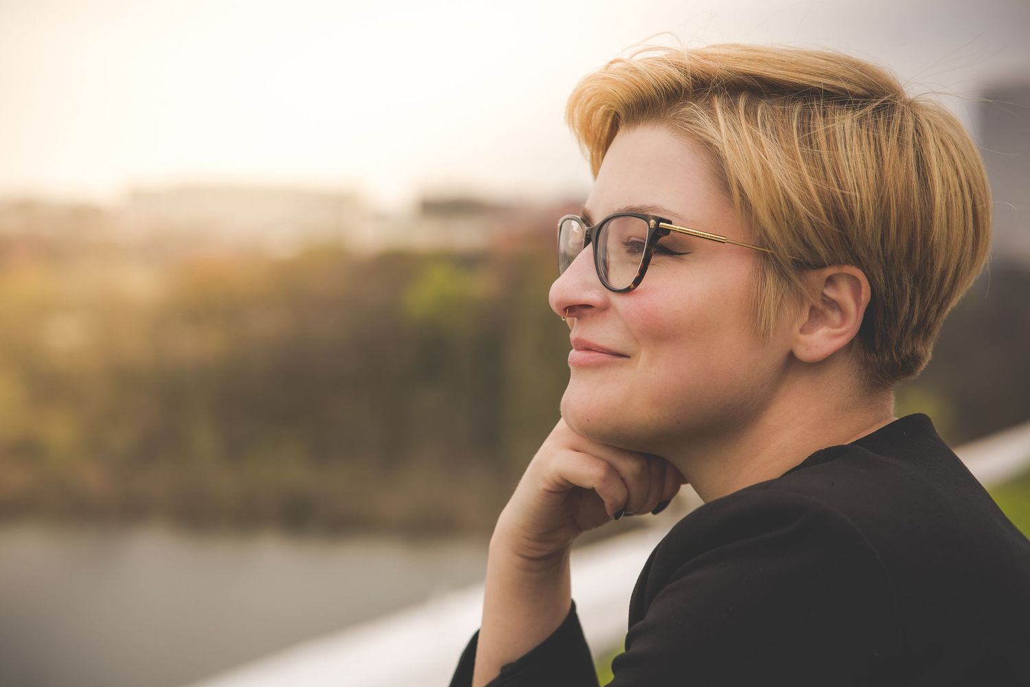 Warm sunset portrait with glasses and black attire in contemplative pose.
