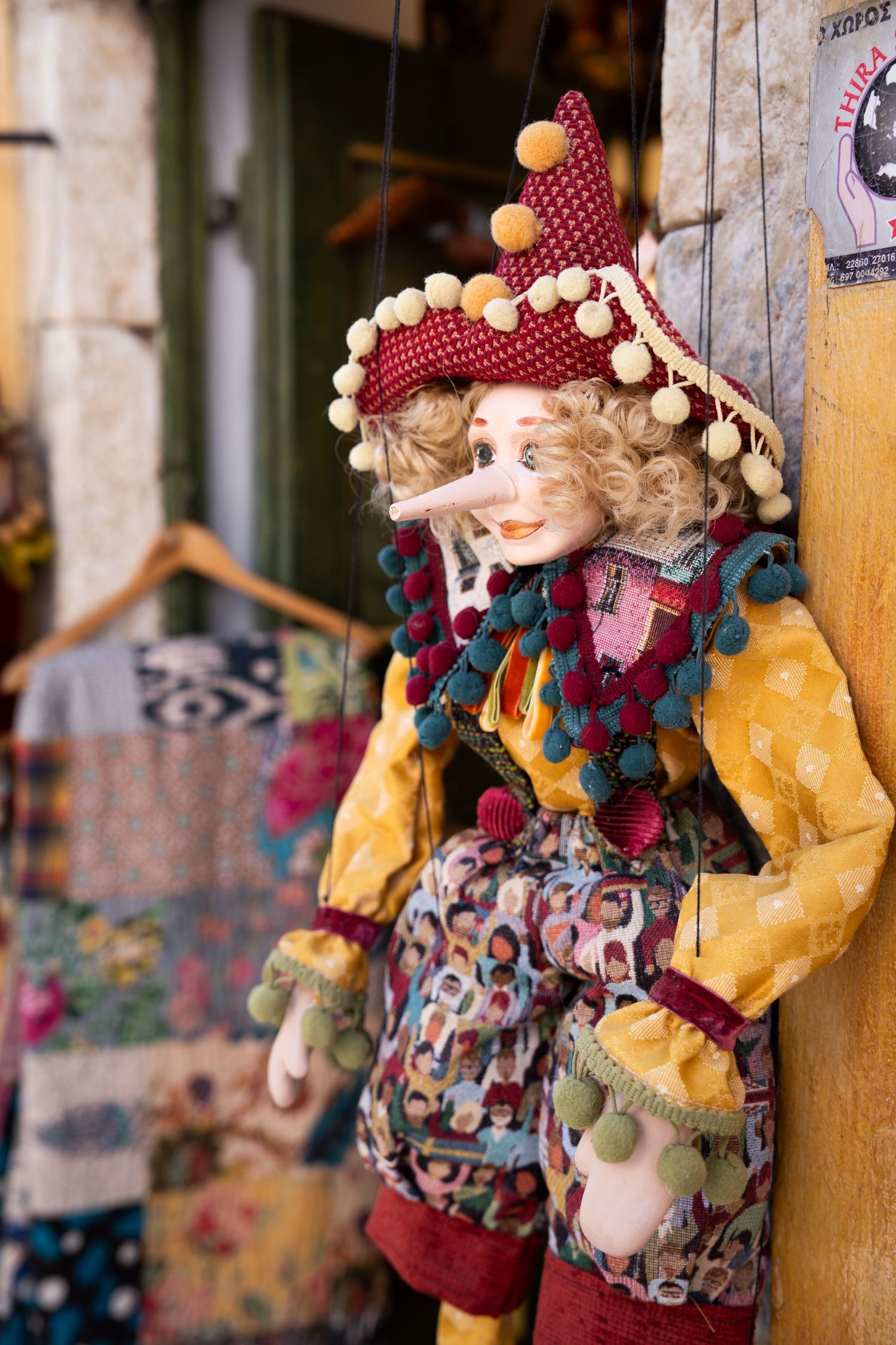 Colorful decorative jester doll with red hat and pom poms hanging on display.