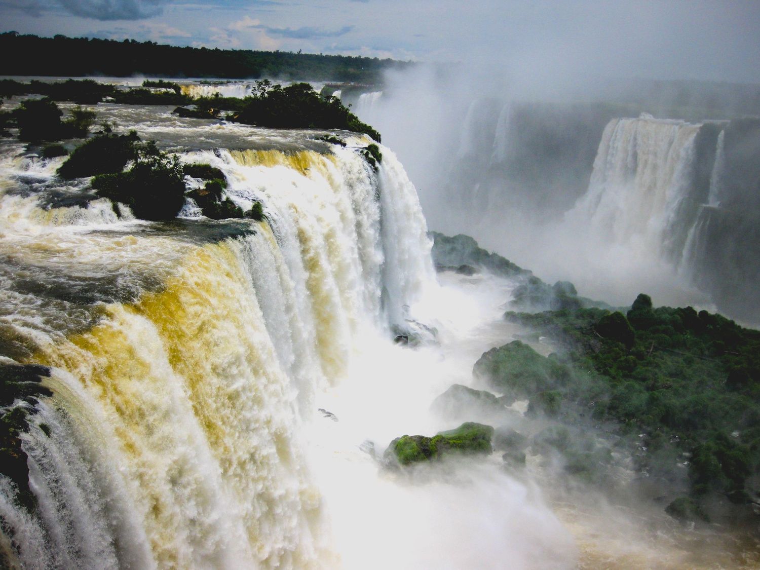Series of massive waterfalls cascading through lush landscape with rising mist and dramatic lighting.