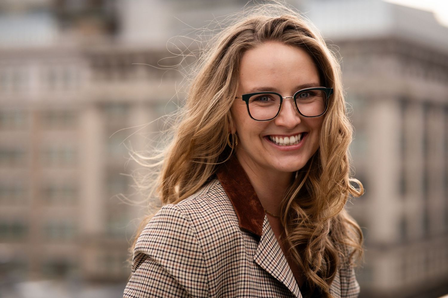 Outdoor professional photo series showing someone in a plaid blazer with city buildings behind.