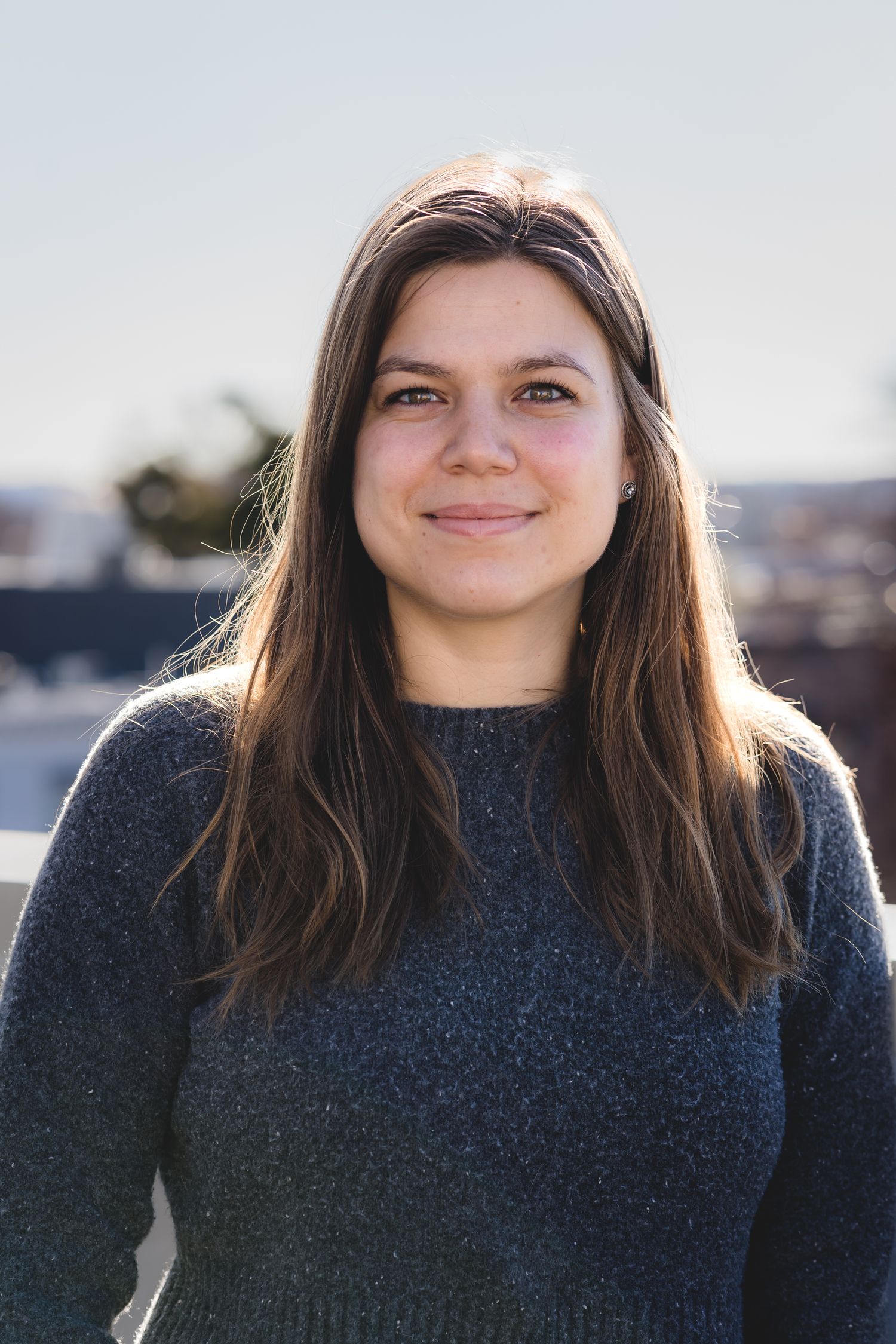 Woman in navy sweater smiling outdoors on rooftop during golden hour.