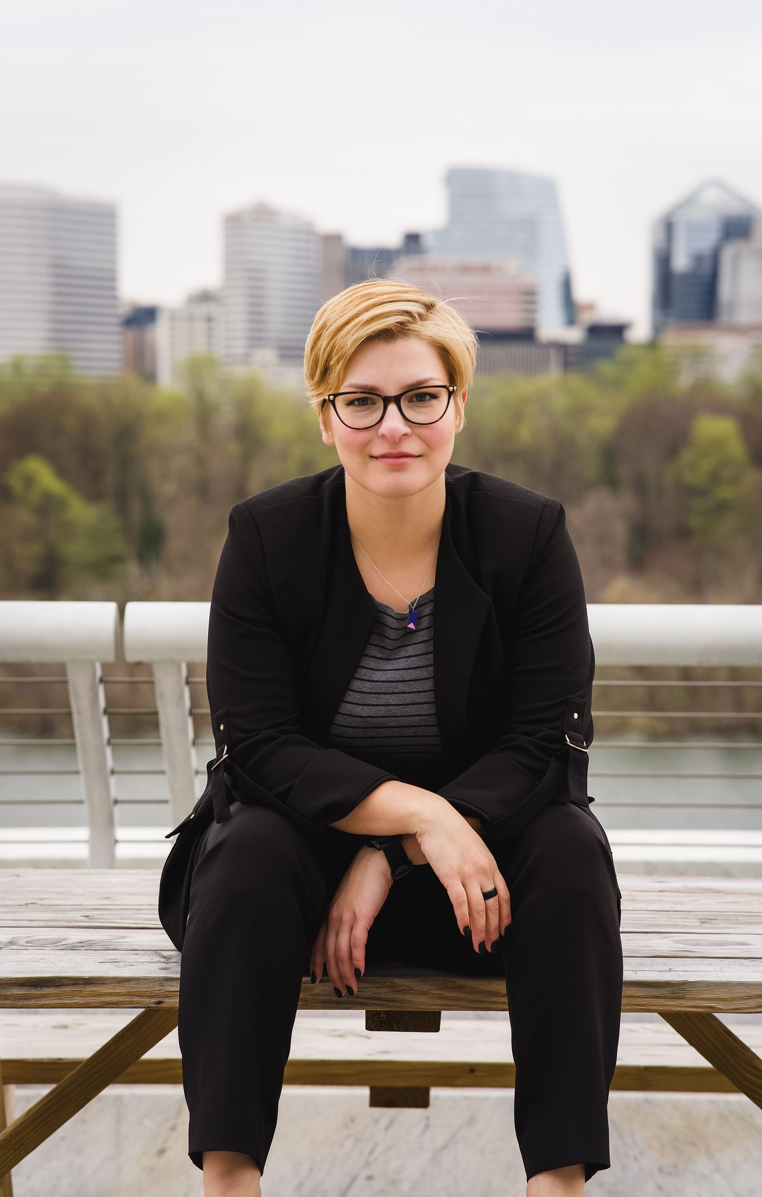 Professional seated portrait on bench with city skyline backdrop.