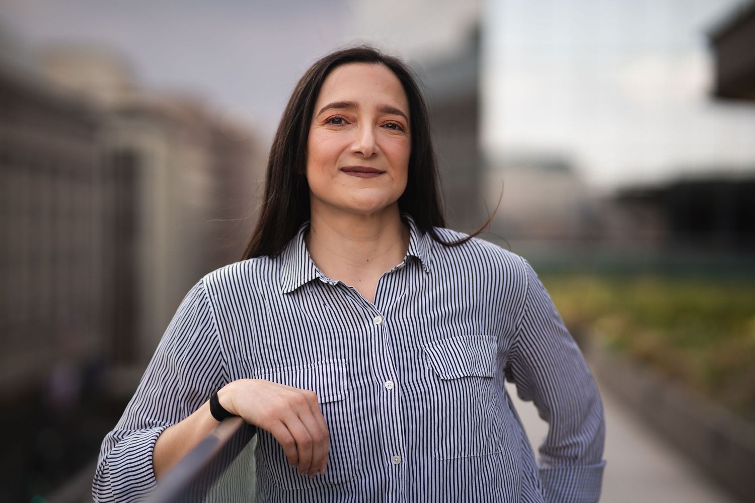 Person wearing pinstriped button-down shirt poses near urban architecture.