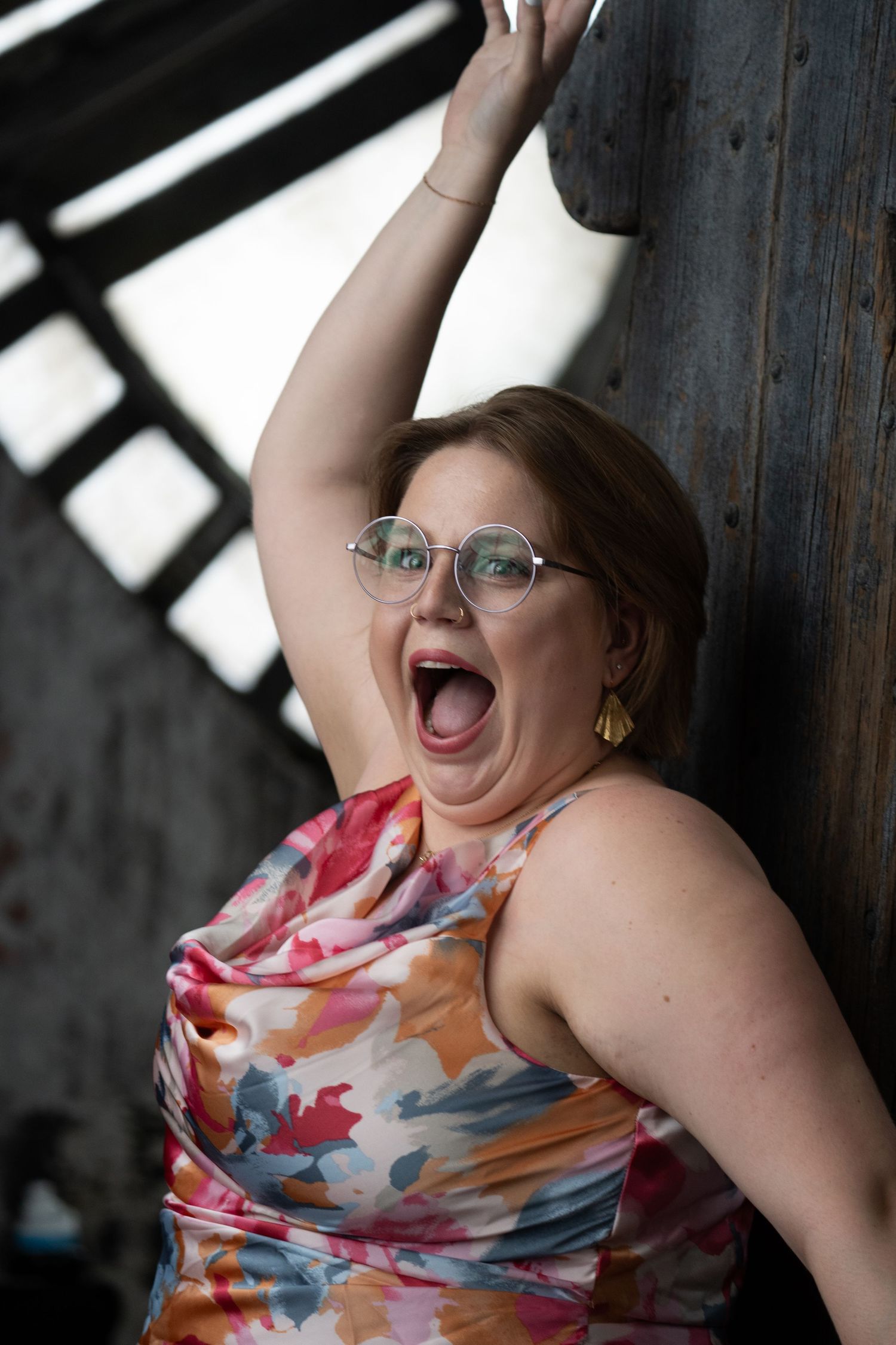 Person in a colorful floral dress poses playfully against industrial backdrop.
