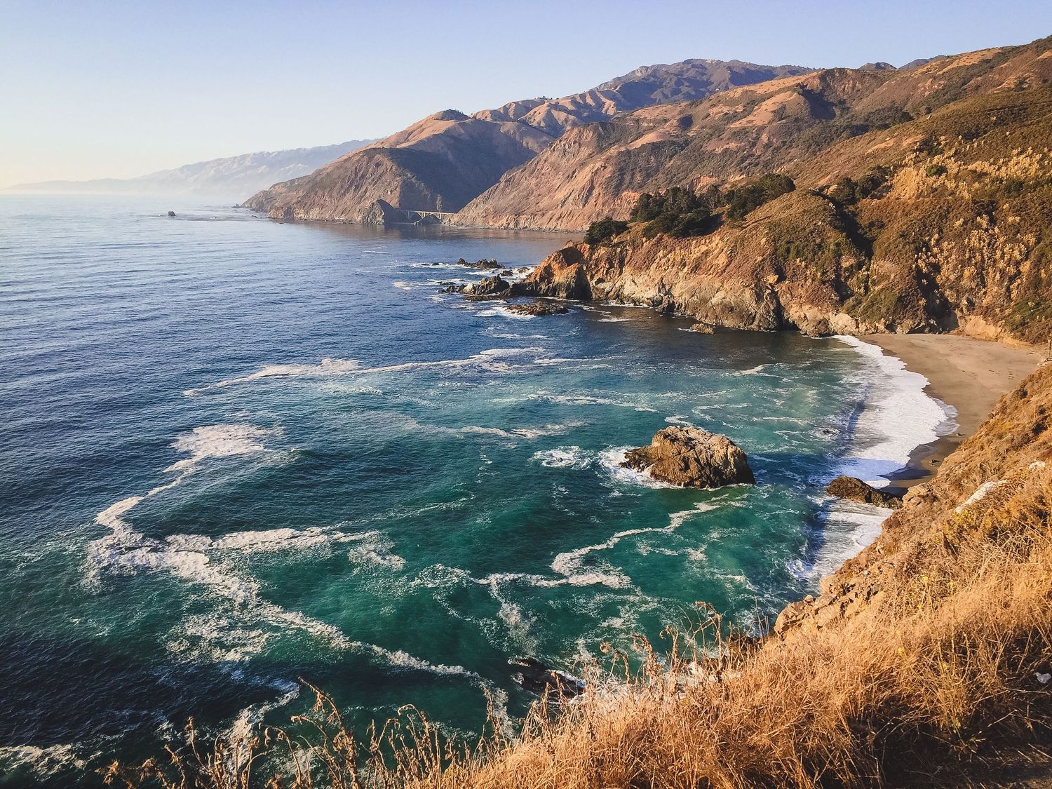 Panoramic view of rocky California coastline with waves crashing against cliffs and sandy beaches.