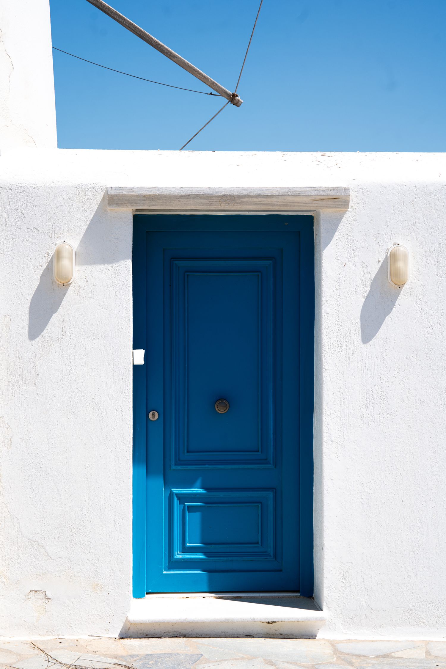 Minimalist architectural detail of bright blue doors against white walls under clear blue sky.