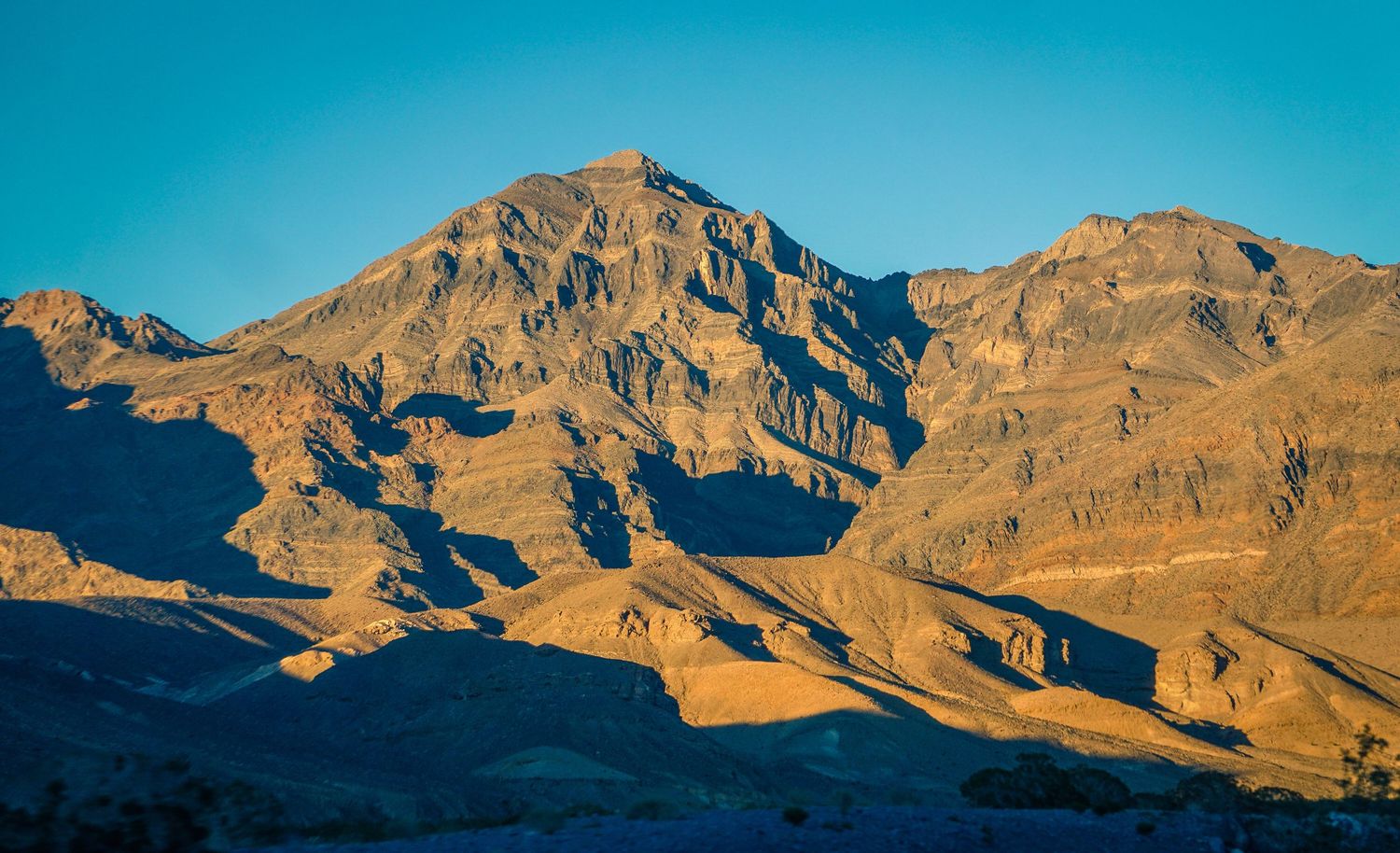 Rugged desert mountain peak bathed in golden afternoon light against clear blue sky.