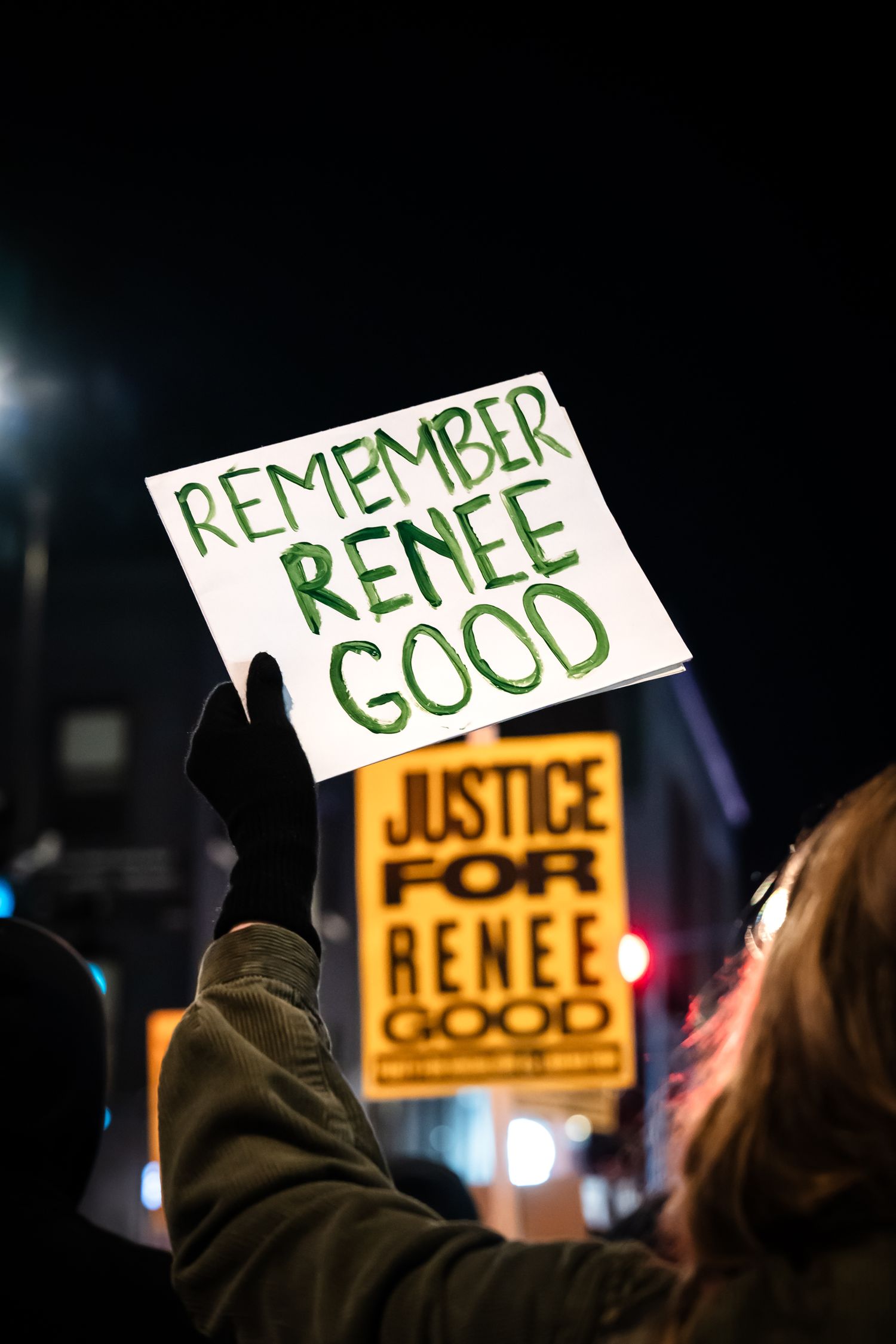 Protest signs held up at night with text reading 'Remember Renee' and 'Justice' illuminated against dark background.
