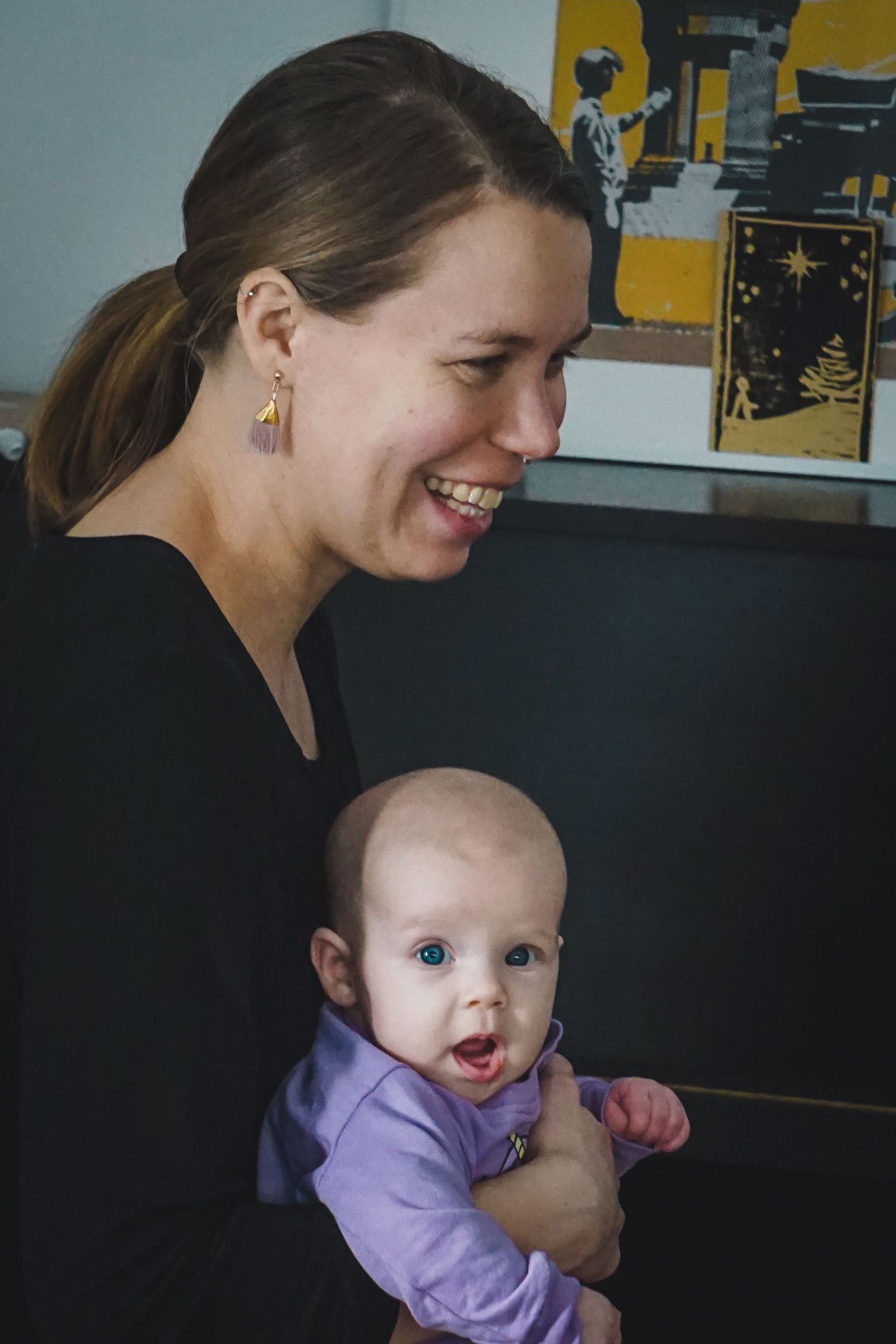 A tender moment captured between a parent in black and a smiling baby wearing purple.
