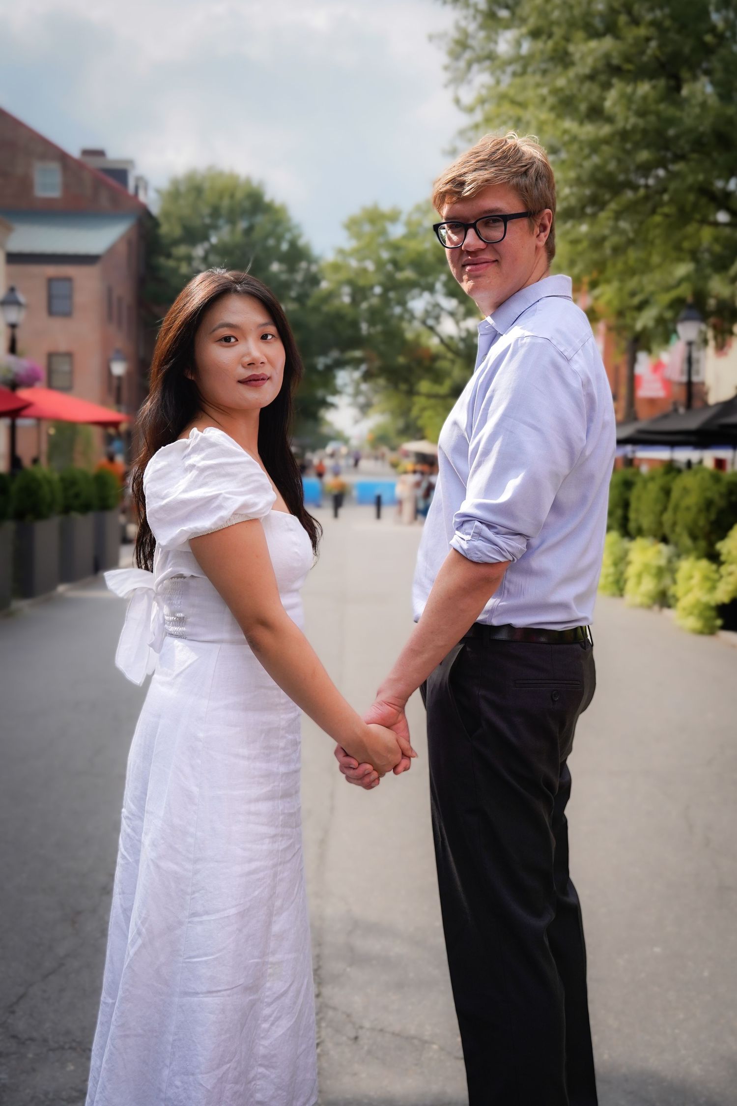 A couple holds hands while walking along a sunny urban pathway.