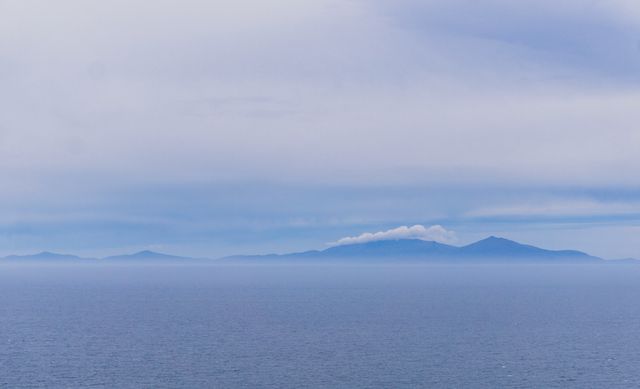 Scenic mountain landscape with misty clouds rolling over distant peaks against a blue sky.