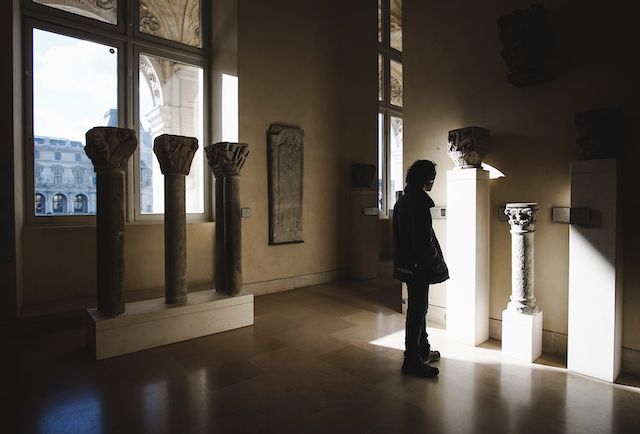 Dramatic shadows and light beams stream through windows in a minimalist gallery space.