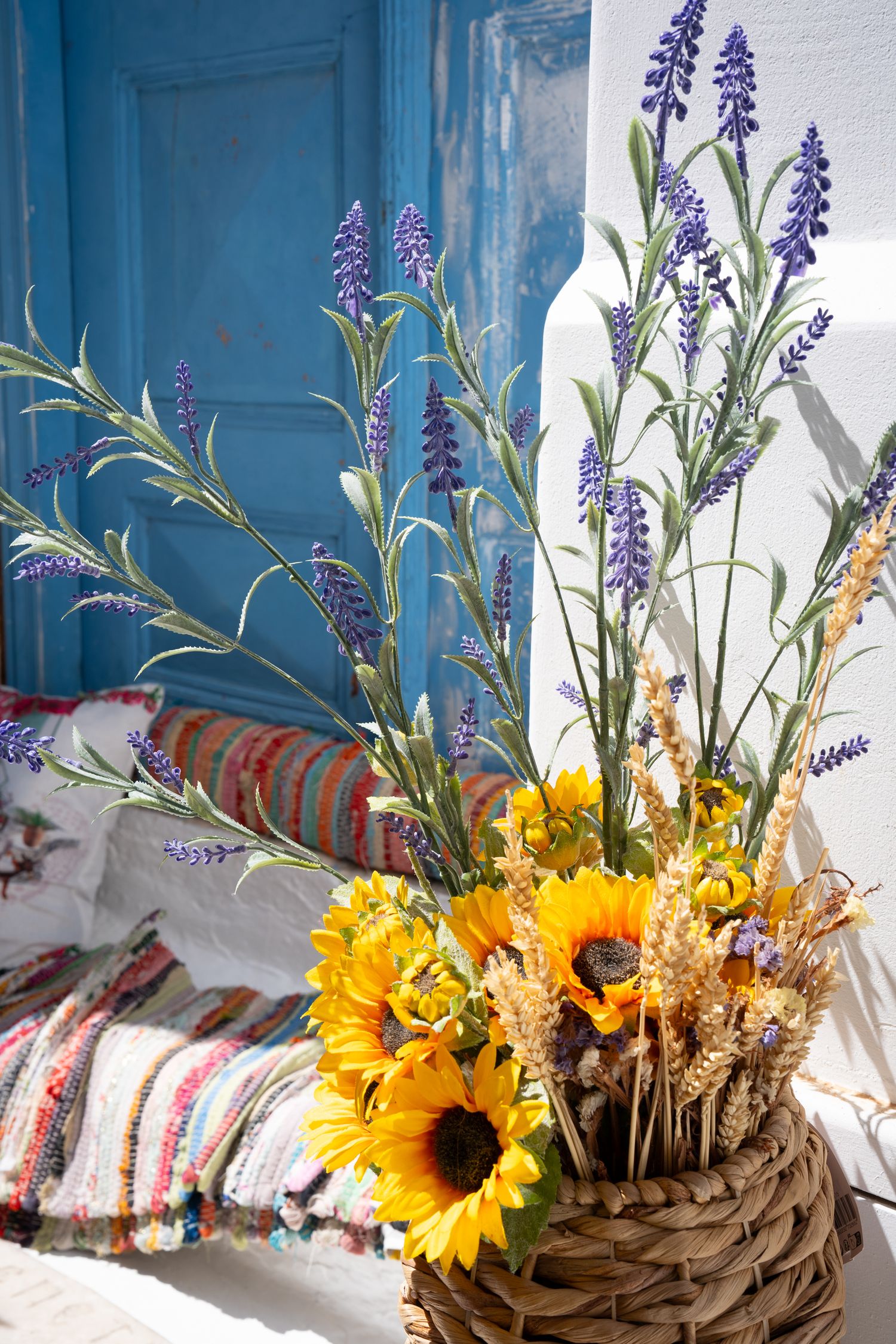 Colorful arrangement of sunflowers and purple flowers against blue door and white wall.