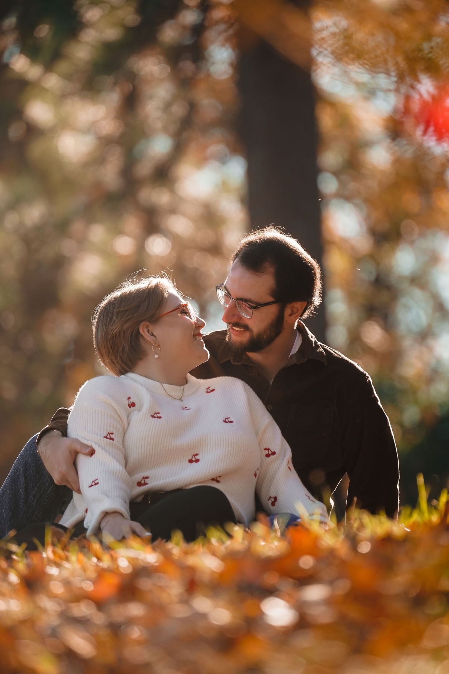 A couple laughs together while lying in golden autumn leaves.