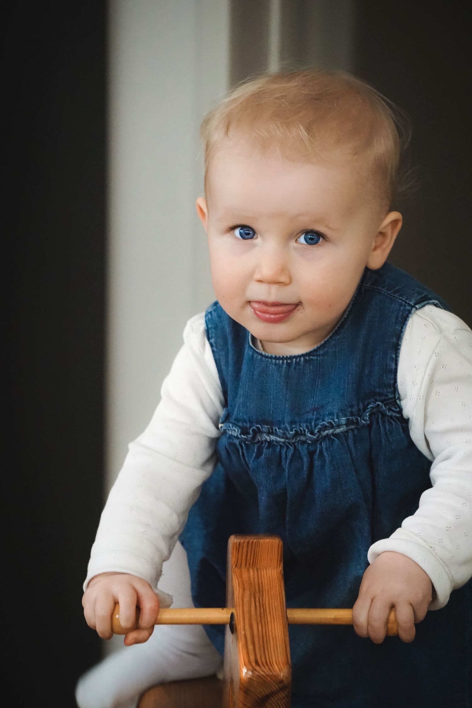 Baby in denim dress sitting on a wooden rocking horse